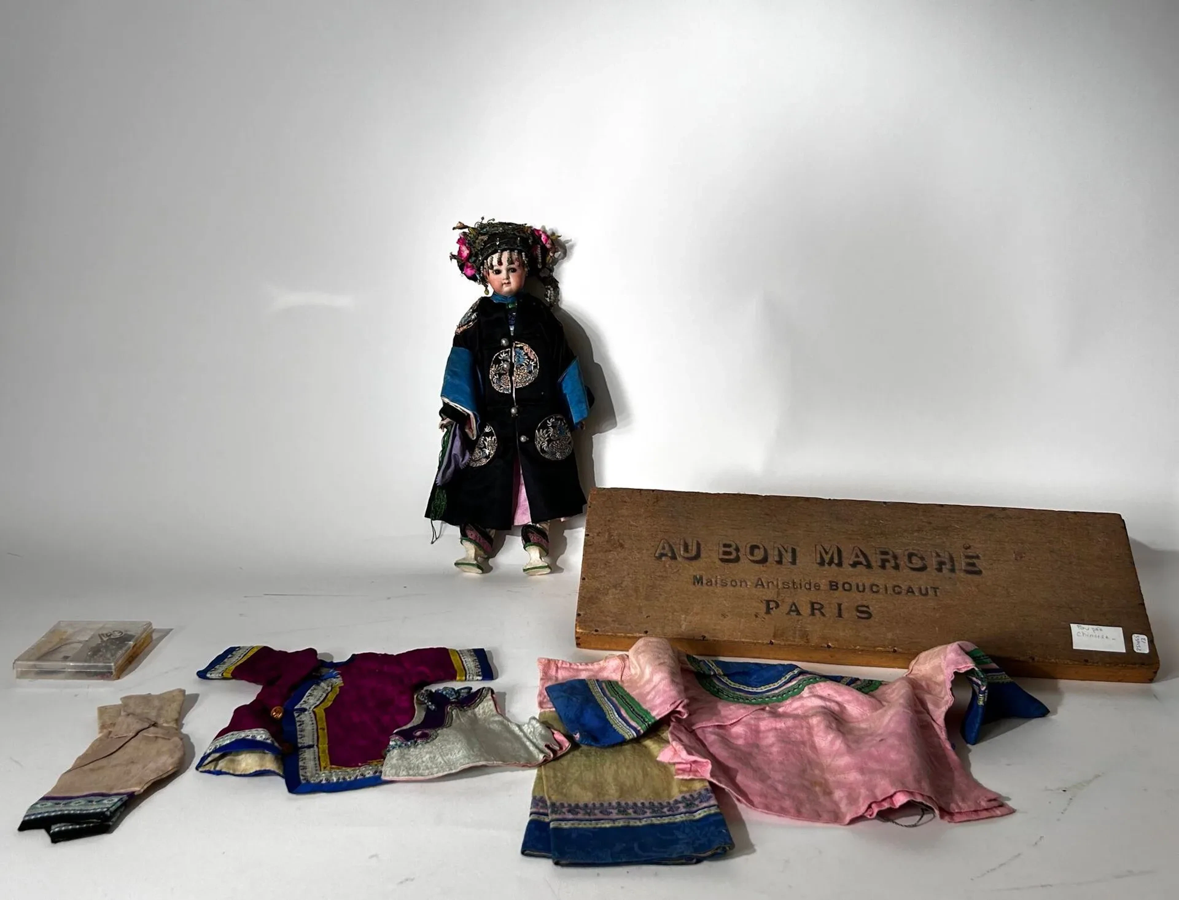 Poupée "chinoise", tête en porcelaine avec ses habits traditionnels et autres vêtements Dans une boite en bois estampillée "Au Bon Marché / Maison Aristide Boucicault / Paris" H : 42 cm Petite restauration à l'oreille