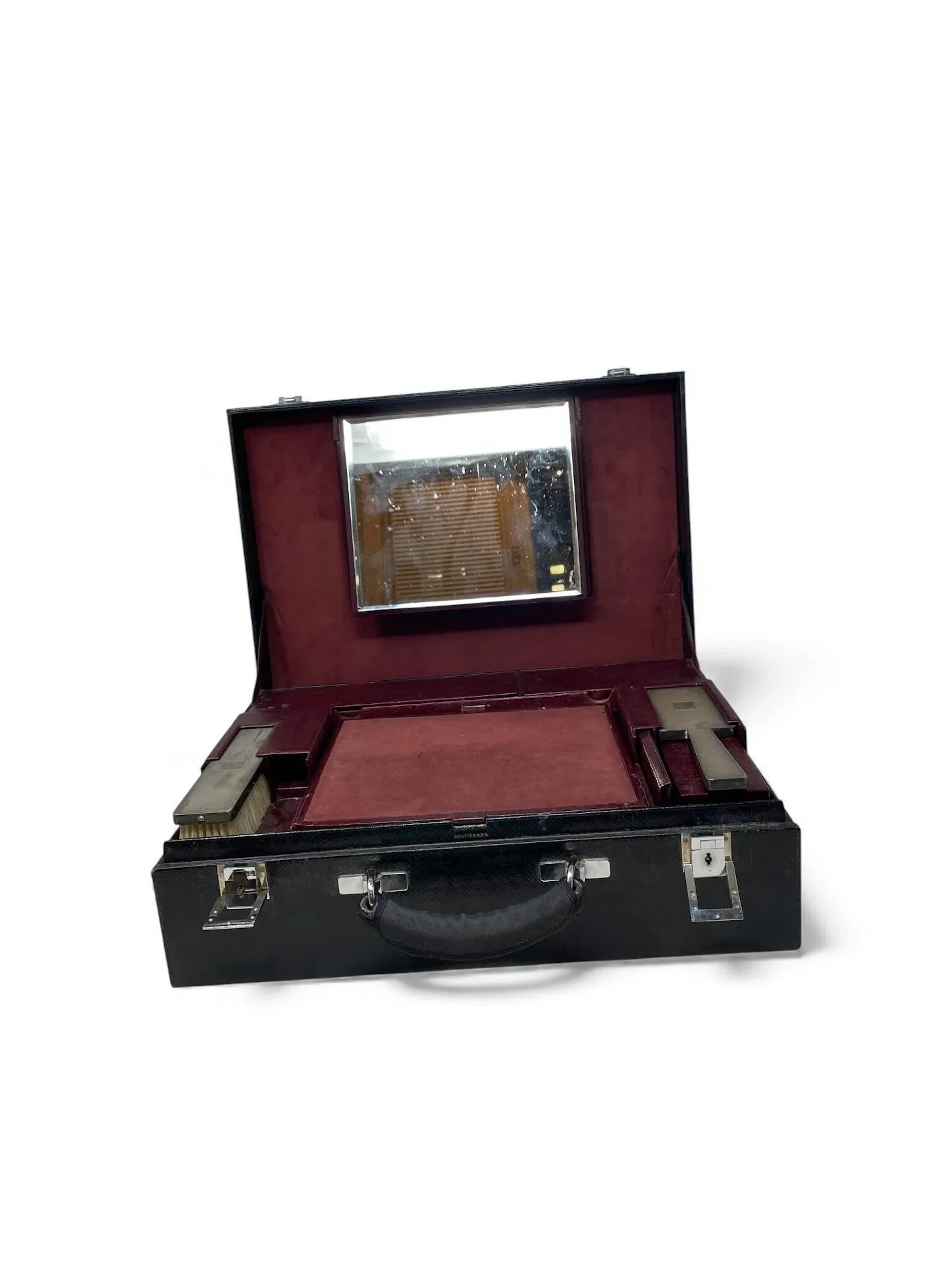 Nécessaire de toilette de voyage rectangulaire en cuir noir découvrant un intérieur en cuir bordeau composé de deux plateaux mobiles agrémentés de trois compartiments fermés, une boîte à bijoux, 9 compartiments accueillants des flacons en verre moulé et argent (950), brosses et nécessaire à ongles. Les plateaux coulissants découvrant un compartiment secret. Miroir amovible sur le couvercle. Housse en tissu et cuir monogrammée N.R.H (accidentée). Travail français début XXème siècle Titre: Minerve 1er titre (1838-1973), Orfèvre: EP différent chat (certainement pour Elie Petit 1909-1931) Poids brut: 510,7 gr Avec les clefs Usures et accidents au cuir, manque certains éléments
