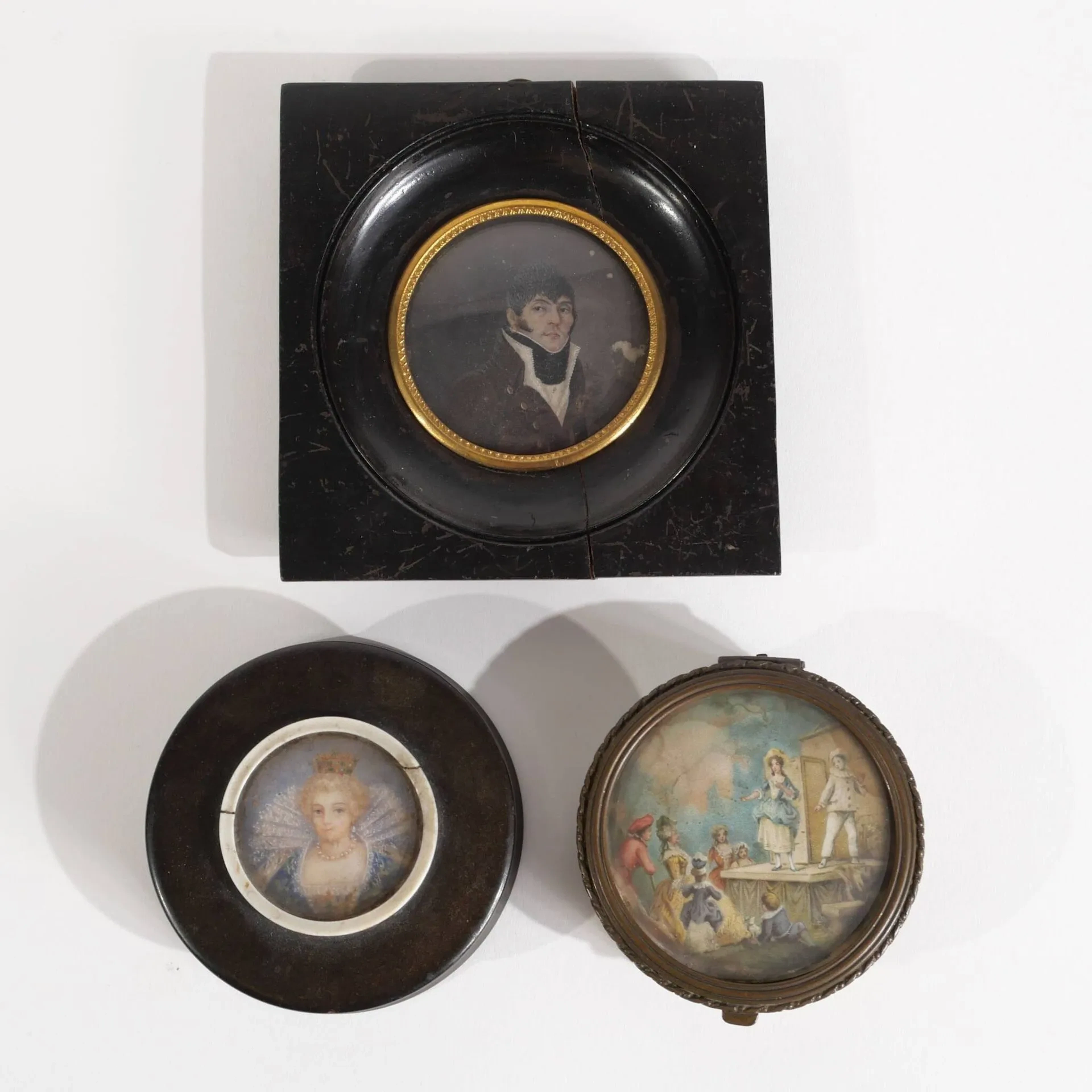 Ensemble de trois objets de vitrine comprenant : -Boite ronde en écaille au couvercle décoré d'un portrait peint d'une noble dame Diam : 8,3 cm -Boite ronde en métal au décor d'une frise de fleurs en ceinture et d'une scène de théâtre (Pierrot) sur le couvercle à charnière Diam : 7,5 cm -Portrait miniature "homme à la veste rouge", école du XIXe siècle Diam : 5,5 cm (à vue) Accidents