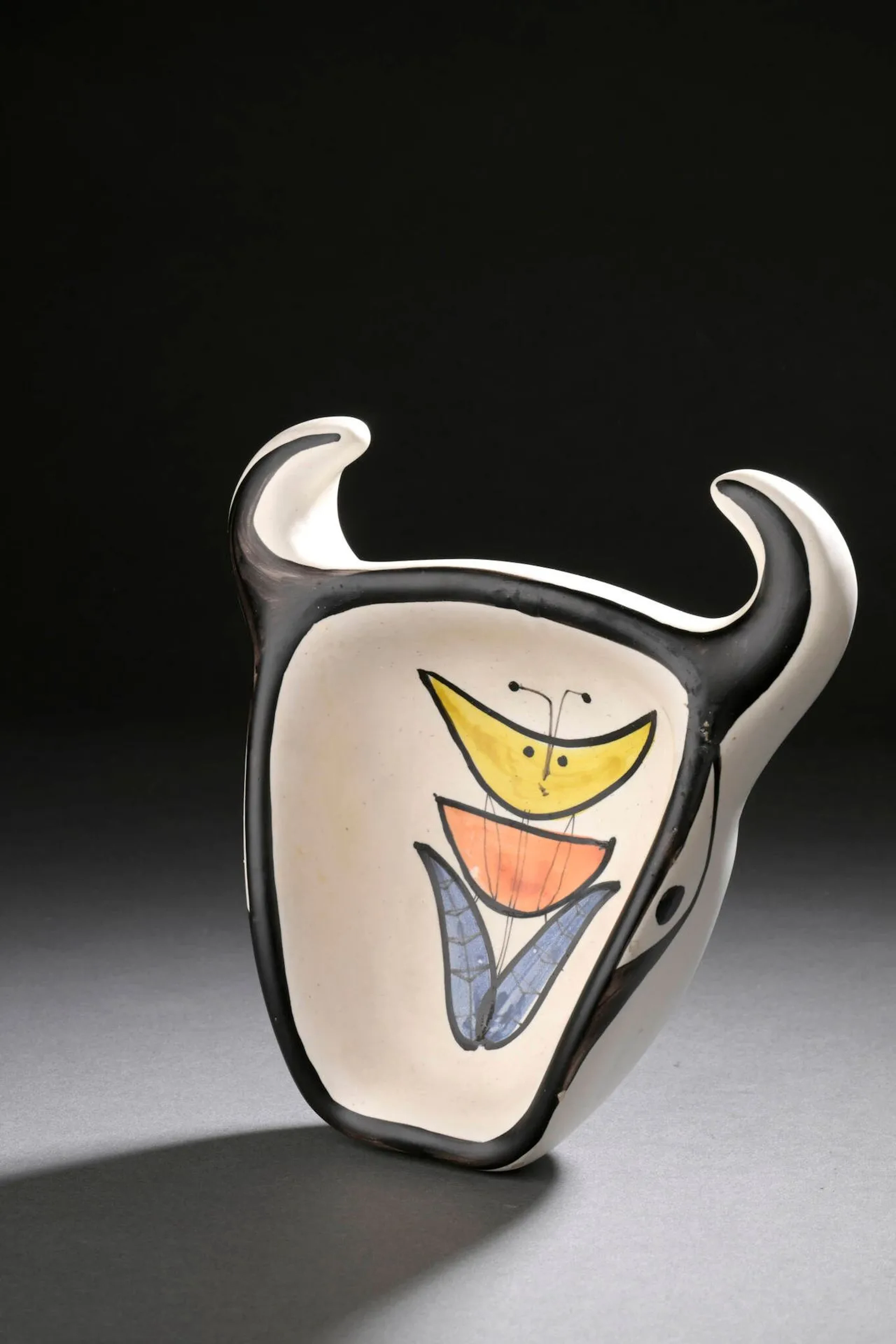 ROGER CAPRON (1922-2006) Cendrier à tête de taureau, circa 1960 Épreuve en faïence émaillée blanc, noir, orange et bleu (Quelques éclats, défauts d’émaillage) H. : 6.3 cm. L. : 18.5 cm. - P. : 17.5 cm. Bibliographie : - Pierre Staundenmeyer, Roger Capron Céramiste, Edition Norma, 2023, modèle similaire reproduit p. 183