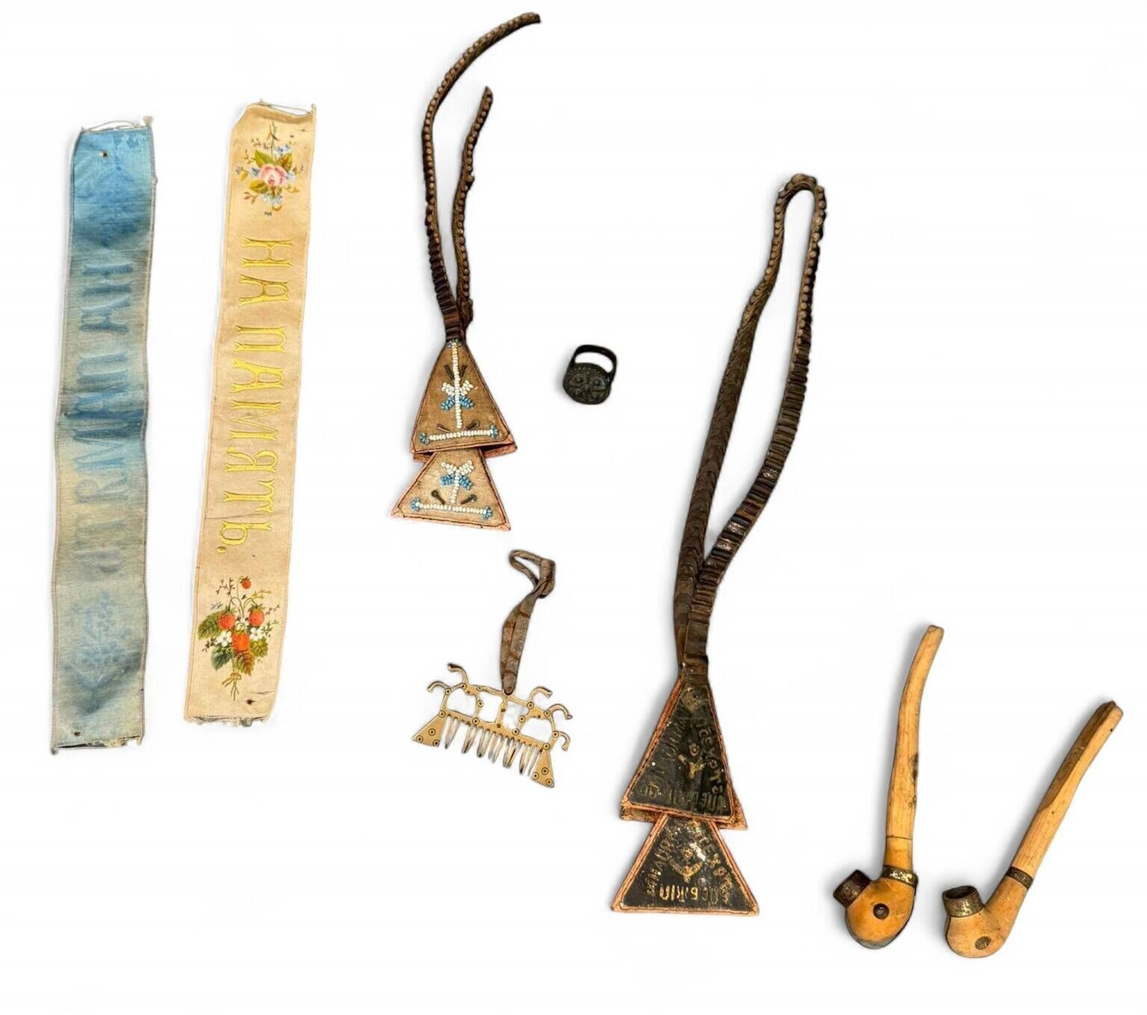 Lot comprenant deux rubans souvenirs inscrits en russe, une bague en cuivre, deux pipes en bois sculpté, un peigne à barbe en laiton, et deux chapelets de vieux croyants (lestovka) en cuir et velours perlé. Usures. Russie, fin du XIXe ou début du XXe siècle.