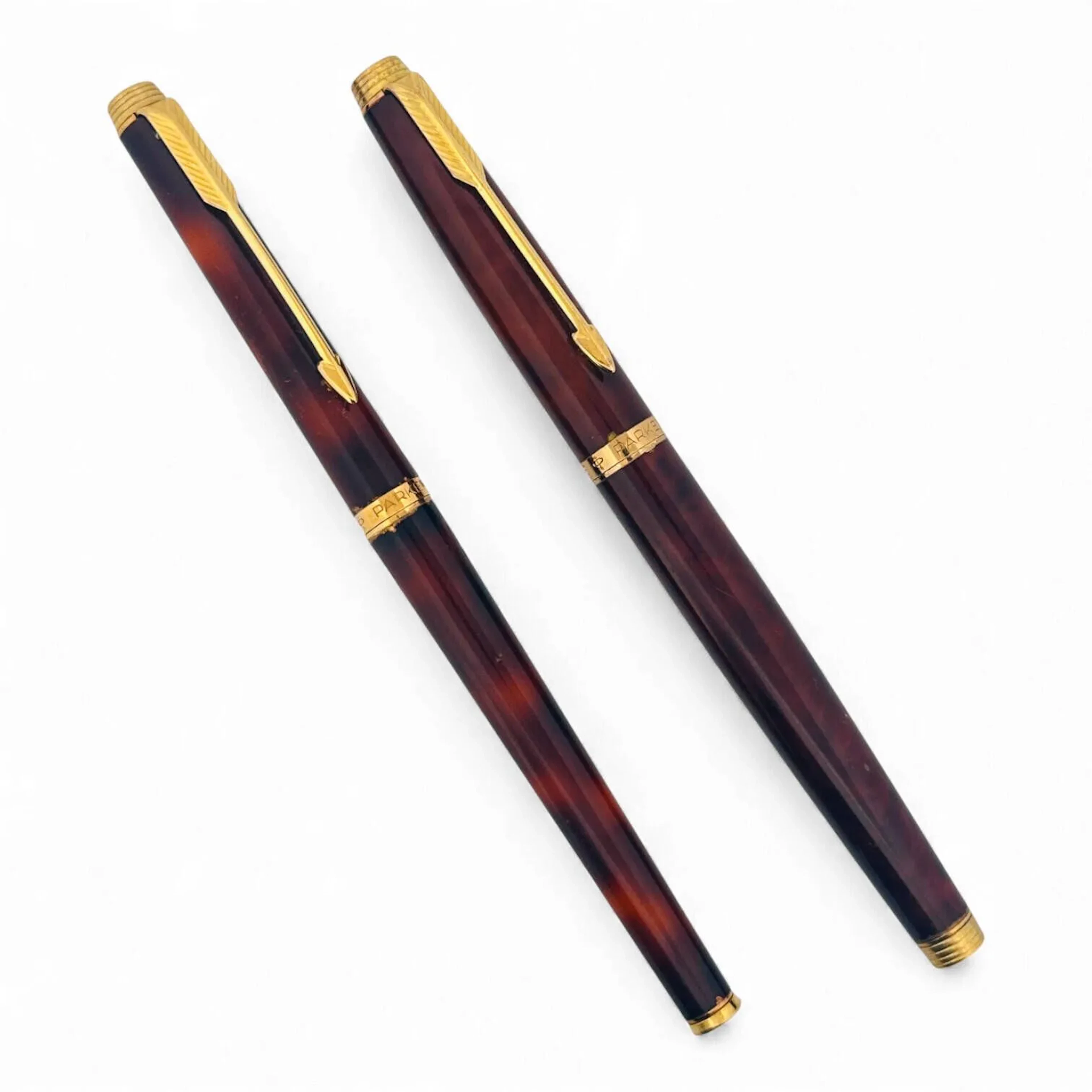PARKER Suite d'un stylo bille et d'un stylo plume en métal doré et laque façon écaille, l'agrafe stylisant une flèche. La plume du stylo en or jaune (750) L. 13 cm Accidents