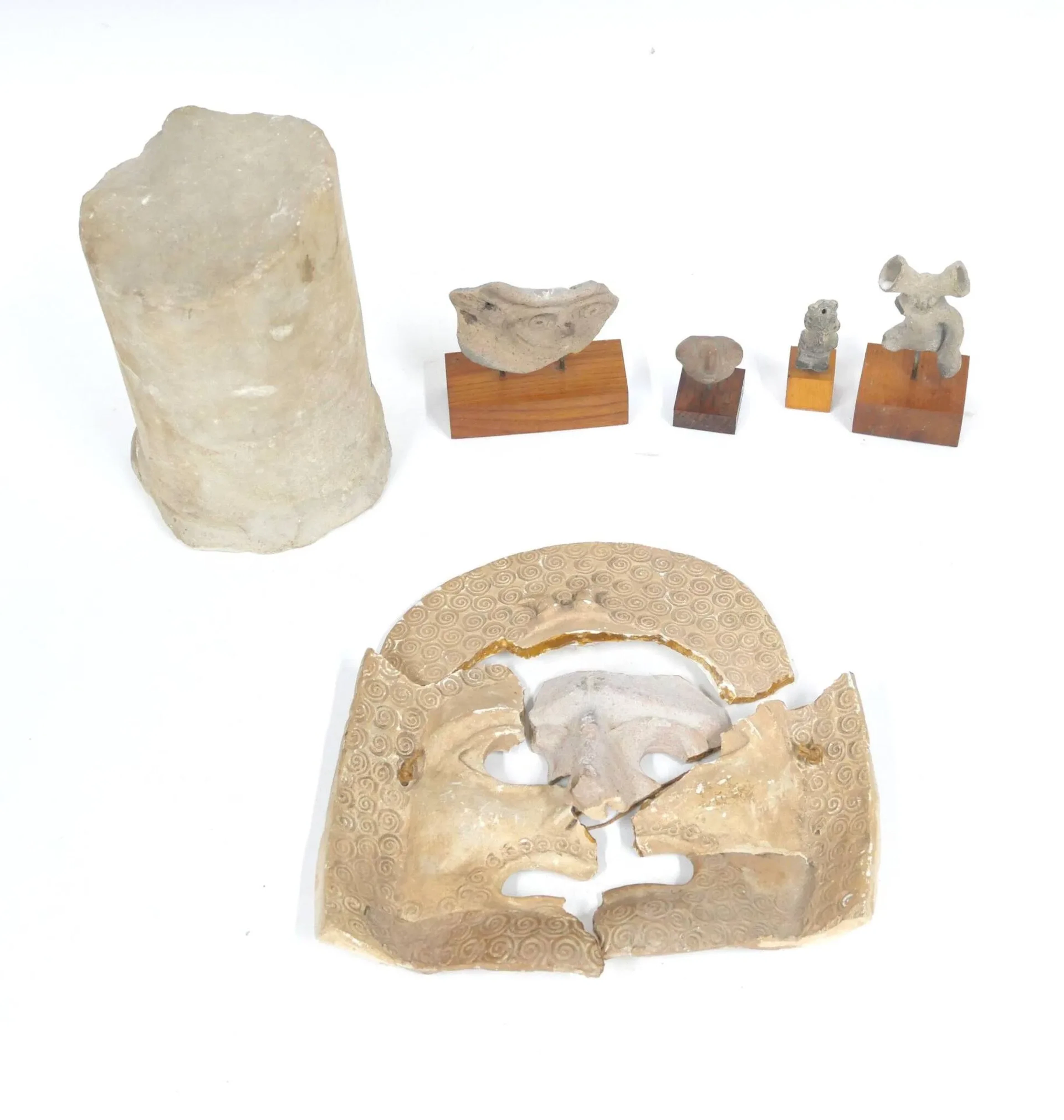 Lot de souvenirs de fouilles archéologiques comprenant - un fragment de colonnette en marbre, H : 20 cm - un masque en terre cuite (à recoller) - quatre petits sujets anthropomorphes en terre cuite sur socle; H du plus grand : 6,5 cm L'ensemble en l'état sans garantie d'époque