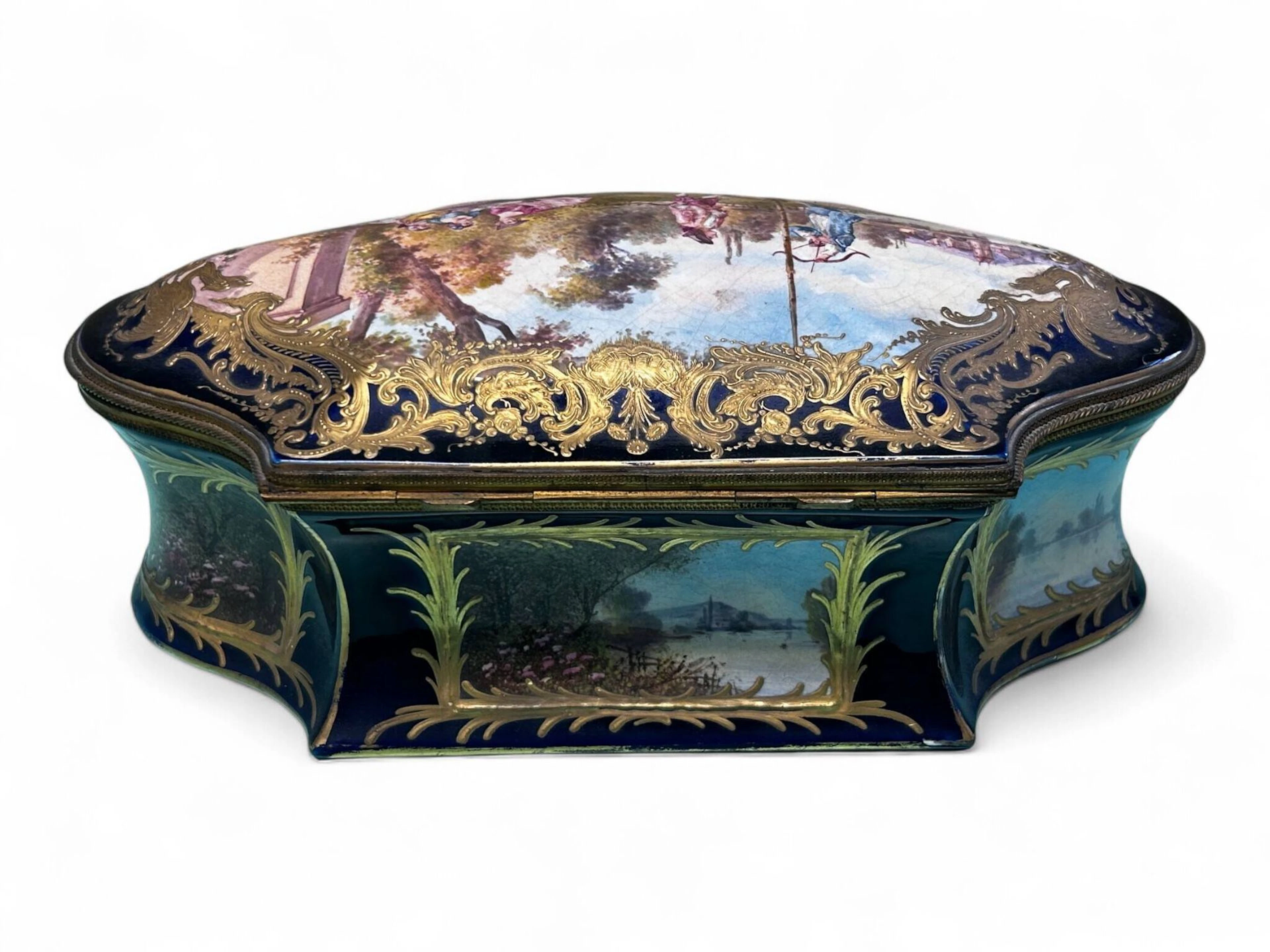 Importante boite couverte en porcelaine à fond bleu de four et à décor polychrome dans un médaillon d'une scène galante dans un encadrement de réhauts d'or, signé LAUQUE. Les bords ornés de paysages. Marque apocryphe de Sèvres sur le dessous avec lettres et inscription "FRANCE" H. 12 - L. 33 - P. 20 cm Usures à la dorure