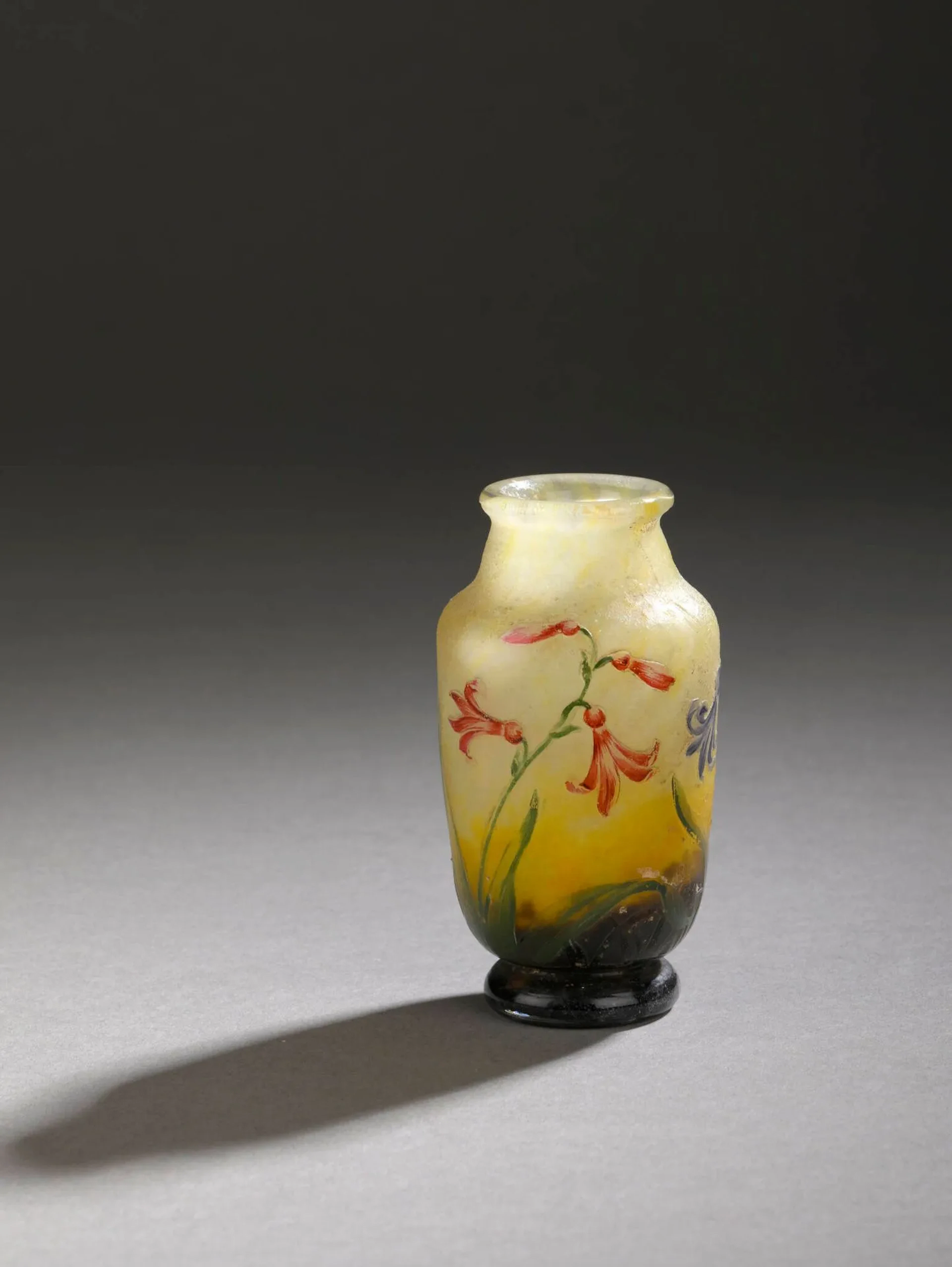 TRAVAIL FRANCAIS XXe Vase à corps ovoïde épaulé et col tubulaire sur petit piédouche. Épreuve en verre marmoréen jaune blanchâtre en partie haute et brun violacé en partie basse. Décor de jacinthes des bois gravé en réserve à l'acide et rehaussé d'émaux polychromes au naturel. signature apocryphe Daum Nancy au revers Haut. 9,5 cm