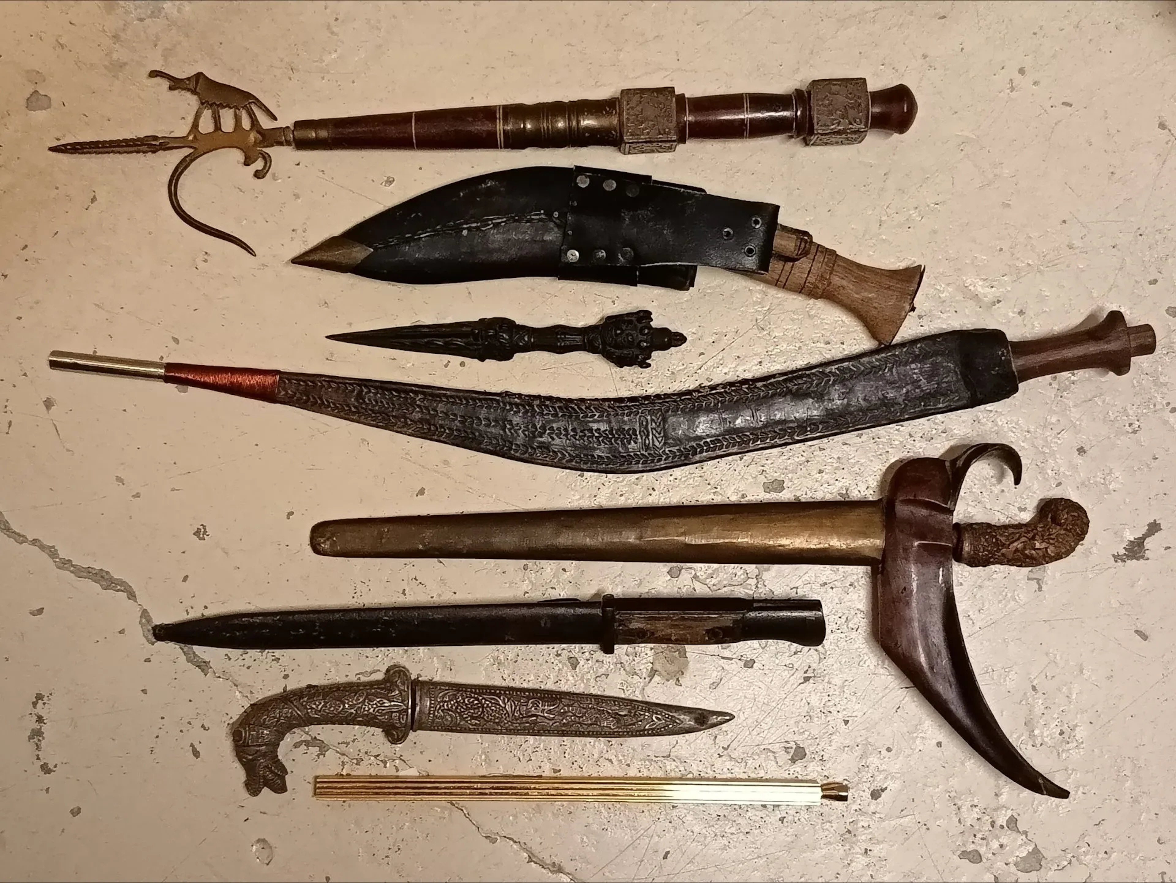 Lot de 8 pièces : Un pique de cornac (fabrication moderne). Un couteau koukri marqué Gopkha army fourreau à âme en bois recouvert de cuir et complet de ses deux petits batardeaux, époque XXe. Un petit poignard indien type rituel en fonte de fer patiné, production moderne. Un poignard courbe d'Afrique du nord, lame brute de forge, fourreau recouvert de peau de chèvre estampée, époque début XXe. Un poignard Kriss malais, monture en matériau composite ciselée, lame flamboyante gravée et fourreau en bois recouvert de feuilles de cuivre ciselé, époque XXe. Une baïonnette pour fusil Mauser 98, fabrication Solingen, plaquettes en bois et fourreau en acier (oxydations). Un couteau décoratif dans le goût asiatique Un coupe papier, en l'état.