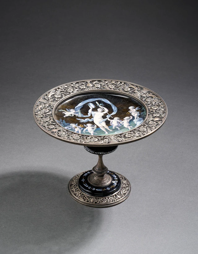 Paul SOYER (1832-1903) Coupé émaillée et en argent (min. 800) sur pied balustre, au décor d'une scène de danse aux angelots musiciens, le pourtour aux rinceaux ajourés Signé à la pointe sous le pied, poinçons d'orfèvre et tête de sanglier H : 13,5 cm; Diam. : 18 cm Poids brut : 506.8 grammes Pied à refixer