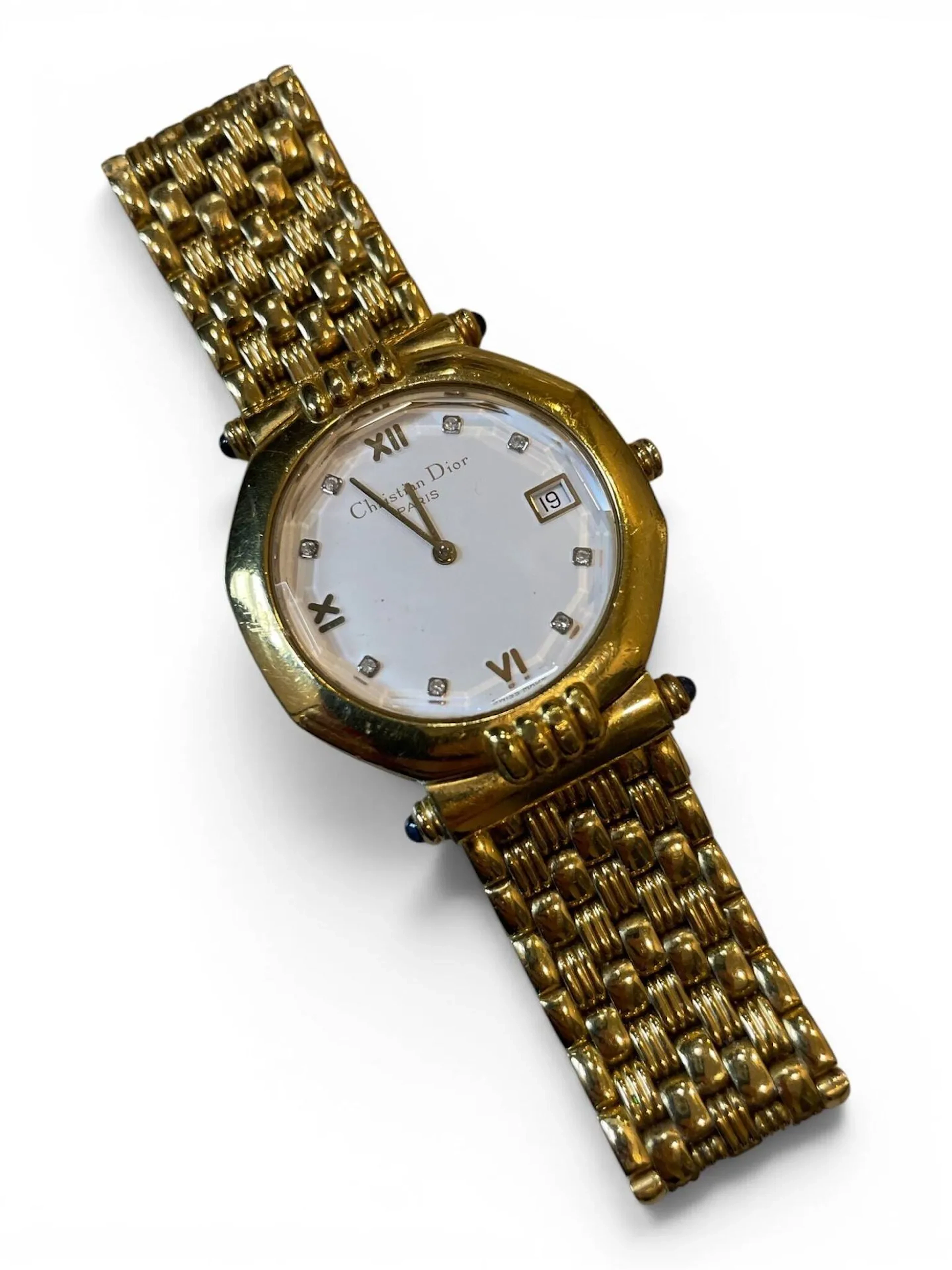 Christian DIOR Montre bracelet en plaqué or à cadran blanc, chiffres romains et index à strass pour les heures, guichet dateur à 3 heures. Fond de boîtier clipsé en plaqué or, signé et numéroté D63 151 AE 9428. Bracelet à mailles articulé en plaqué or à boucle signée. Diam. 33 mm Rayures et oxydations