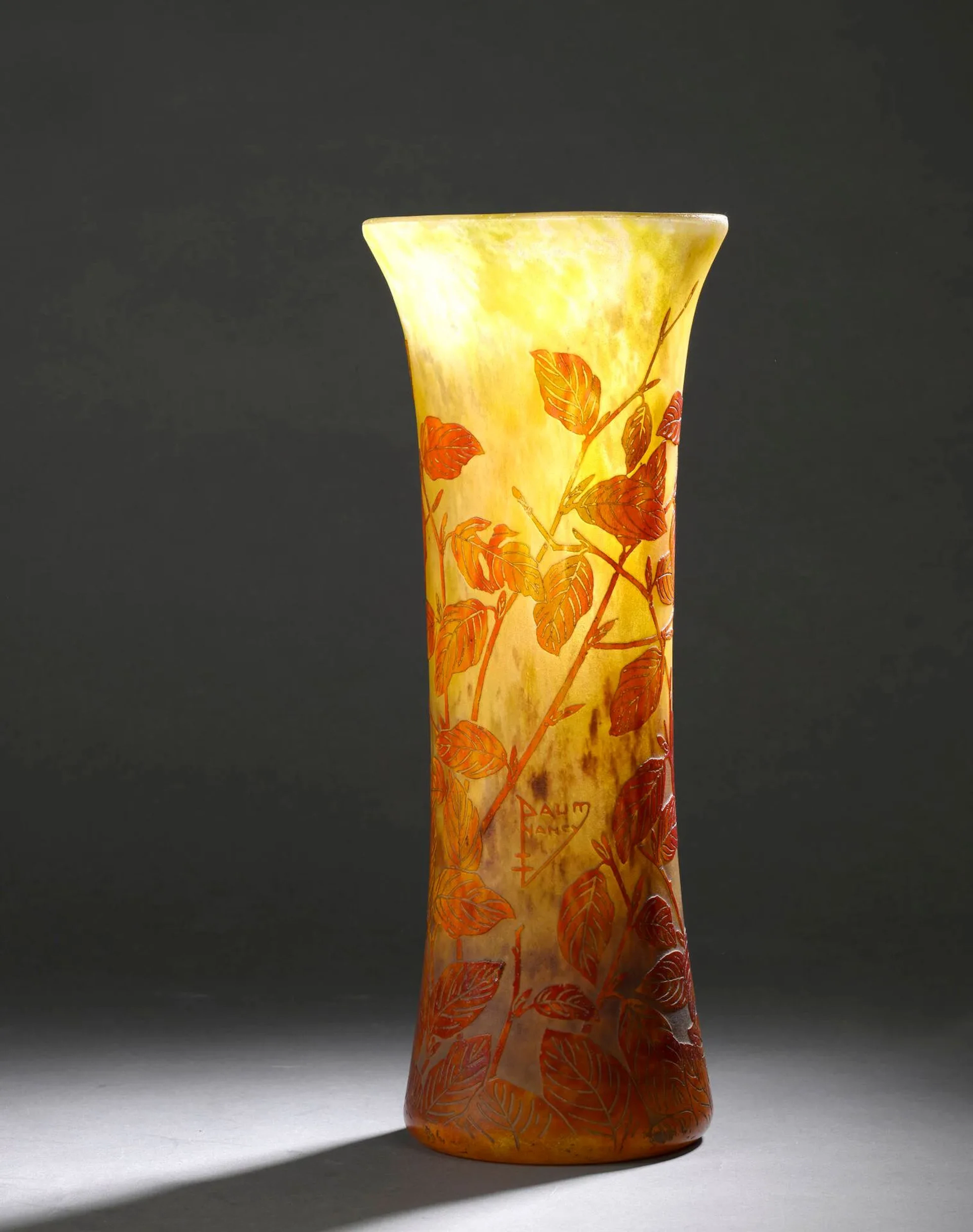 DAUM – NANCY Vase cornet à col conique. Épreuve en verre poudré rouge orangé sur fond marmoréen jaune blanchâtre. Décor de feuilles de frênes gravé en camée à l’acide (une bulle éclatée au col). Signé dans le décor. Haut. 43 cm