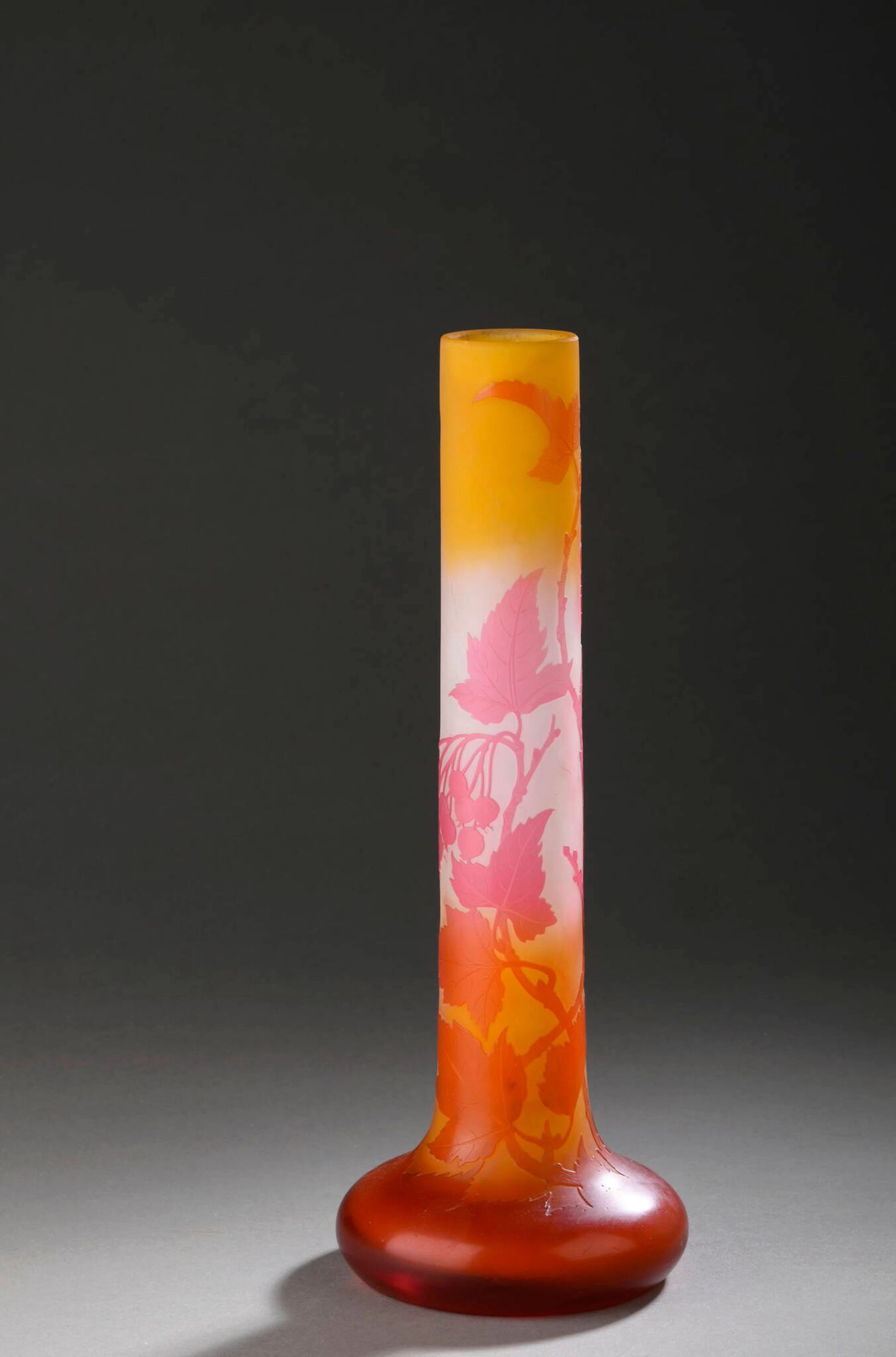 ETABLISSEMENTS GALLE (1904-1936) Soliflore à long col tubulaire sur base ovoïde aplatie. Épreuve en verre multicouche rose et orange sur fond blanchâtre orangé. Décor de baies et de feuilles gravé en camée à l’acide. Signé dans le décor. Haut. 33,5 cm