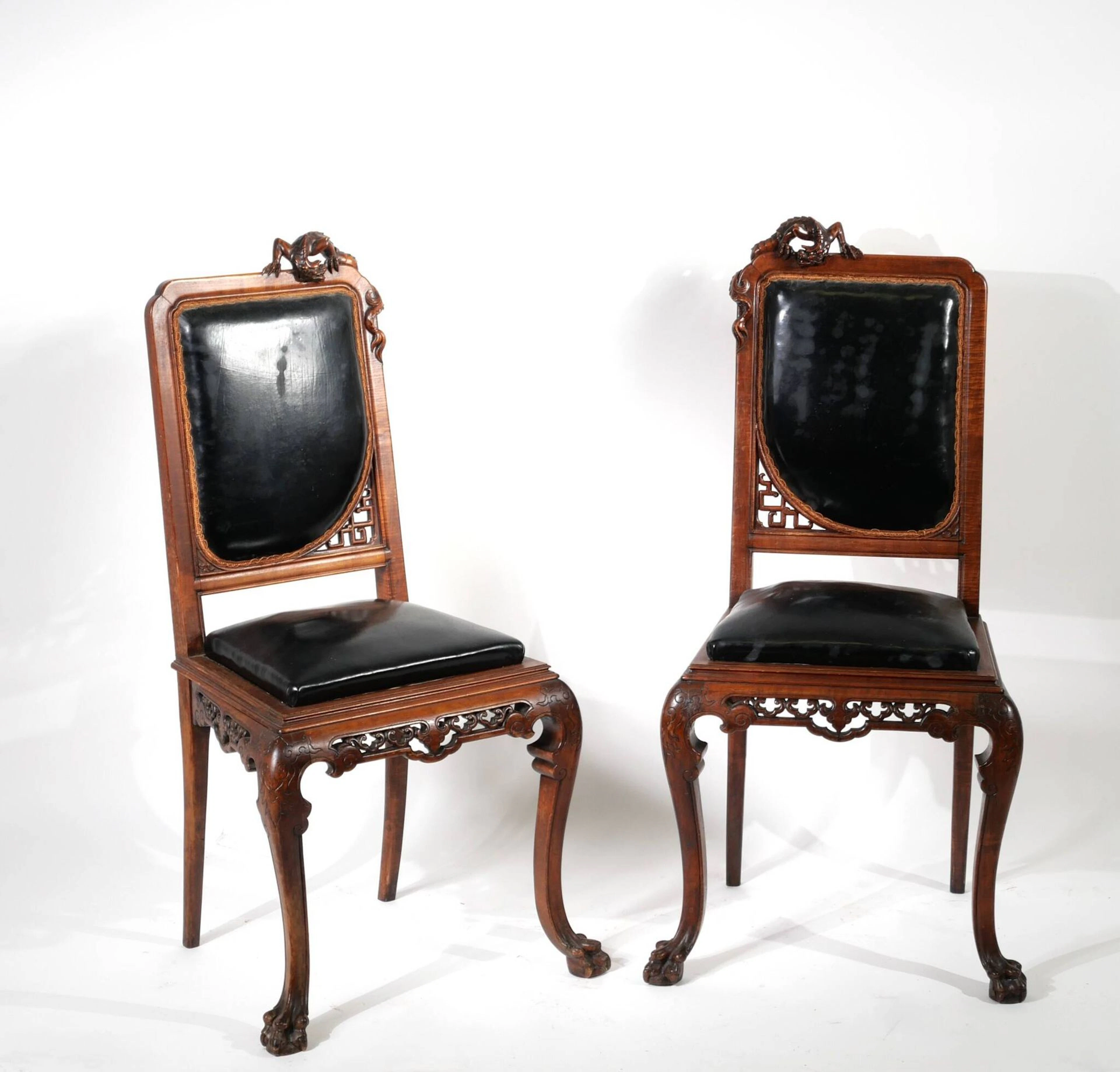 Pair of carved wooden chairs with sinuous forms, topped by a - Lot 129