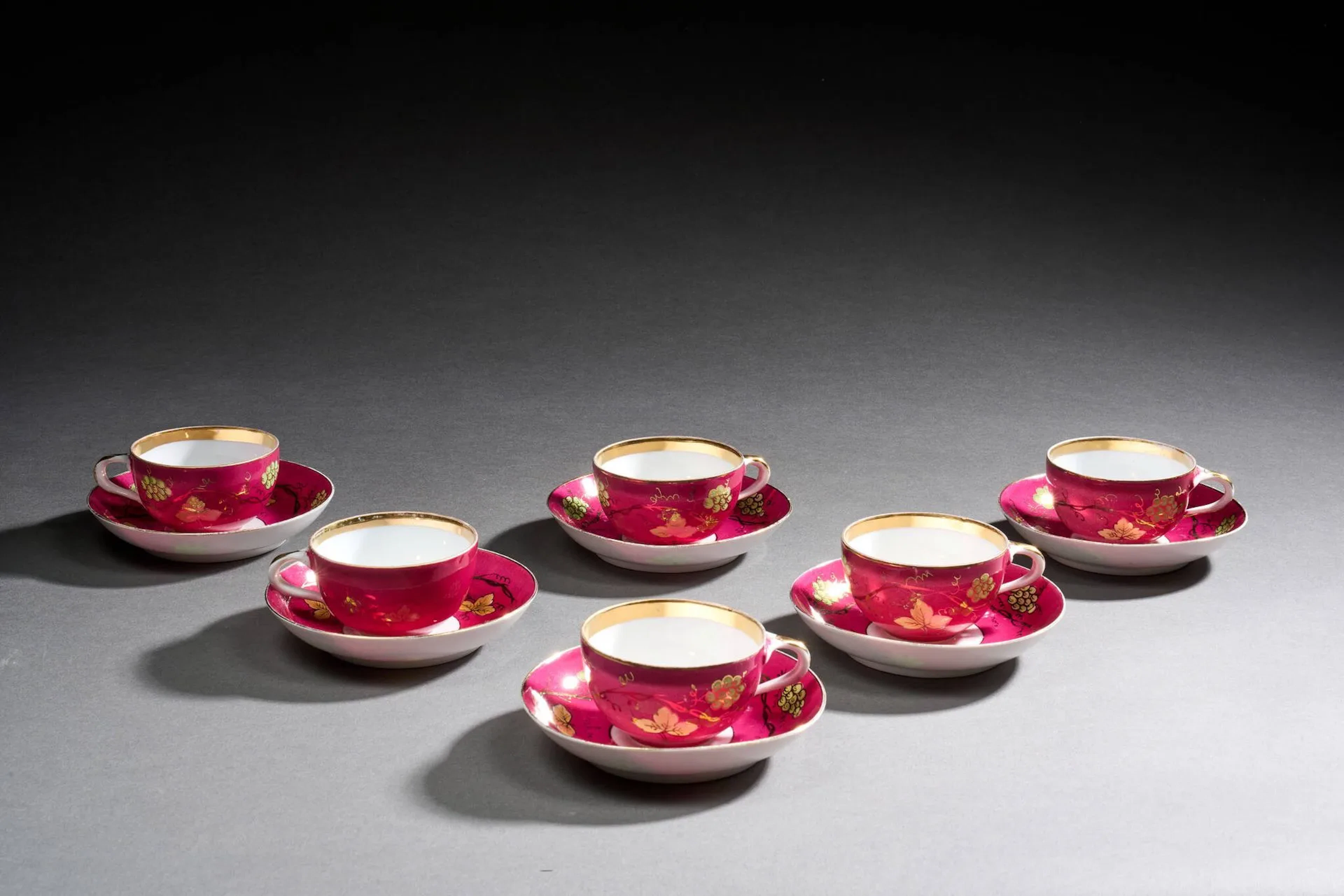 RUSSIE Partie de service à café en porcelaine, comprenant six tasses et leur soucoupe, à fond rose et décor peint en or et vert de pampres de vigne, filet or sur les bords. Petits fêles et usures de l’or. Moscou, manufacture Gardner pour le marché perse, fin du XIXe siècle. Marque au tampon rouge au revers. H. 5,5 x D. 13,5 cm.
