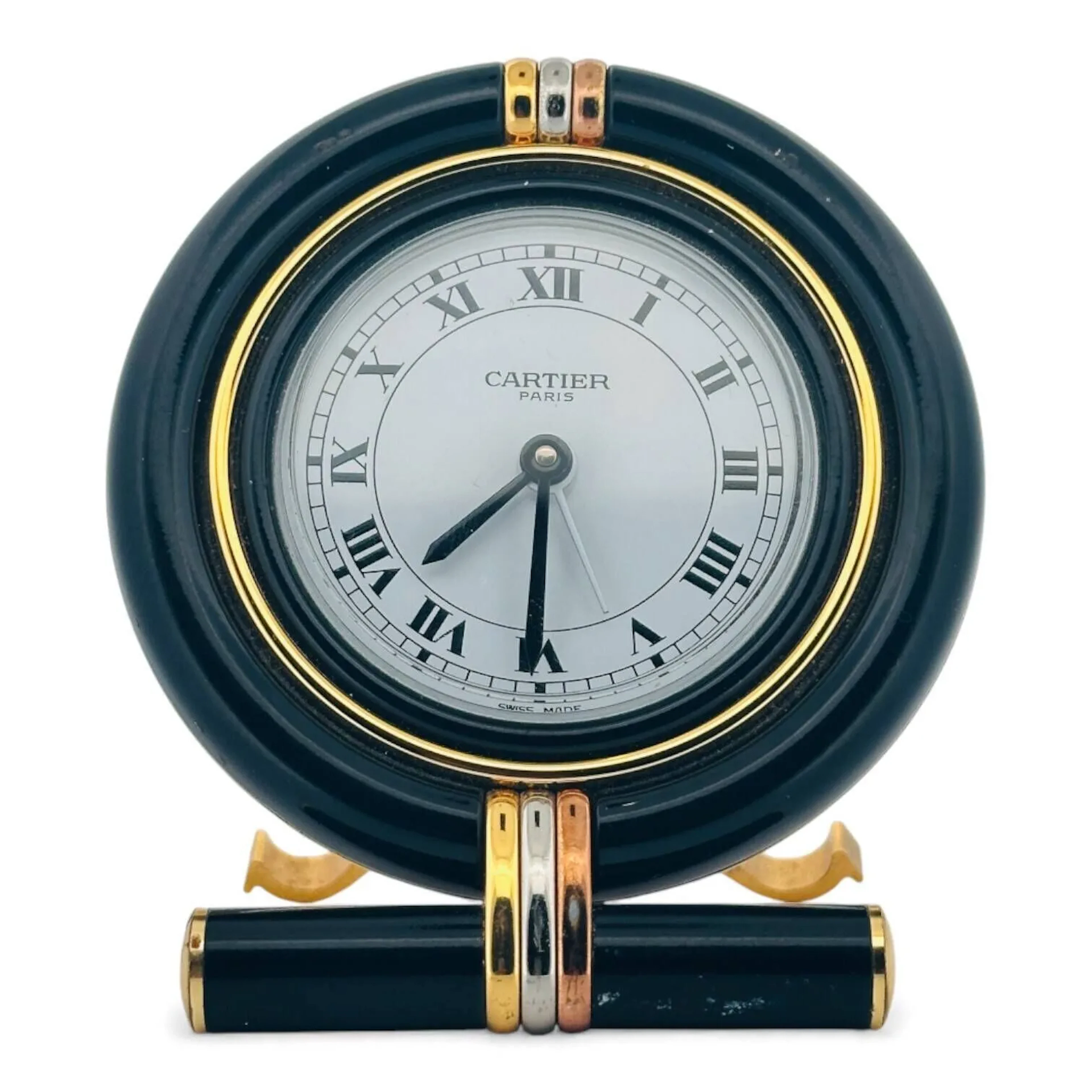 CARTIER Pendulette réveil de table en métal peint et laiton, cadran blanc laqué, minuterie chemin de fer noire, index des heures chiffres romains en décalques noires, aiguilles glaives noires, aiguille de réveil blanche. Lunette peinte noire, socle cylindrique peint noir, métal doré des trois ors Cartier. Le dos signé Cartier, calibre à quartz, support amovible décoré des lettres «C». Pendulette non fonctionnelle lors de l’expertise, sans garantie de fonctionnement futur et d’état des pièces. Vers 1980 Diamètre 75 mm