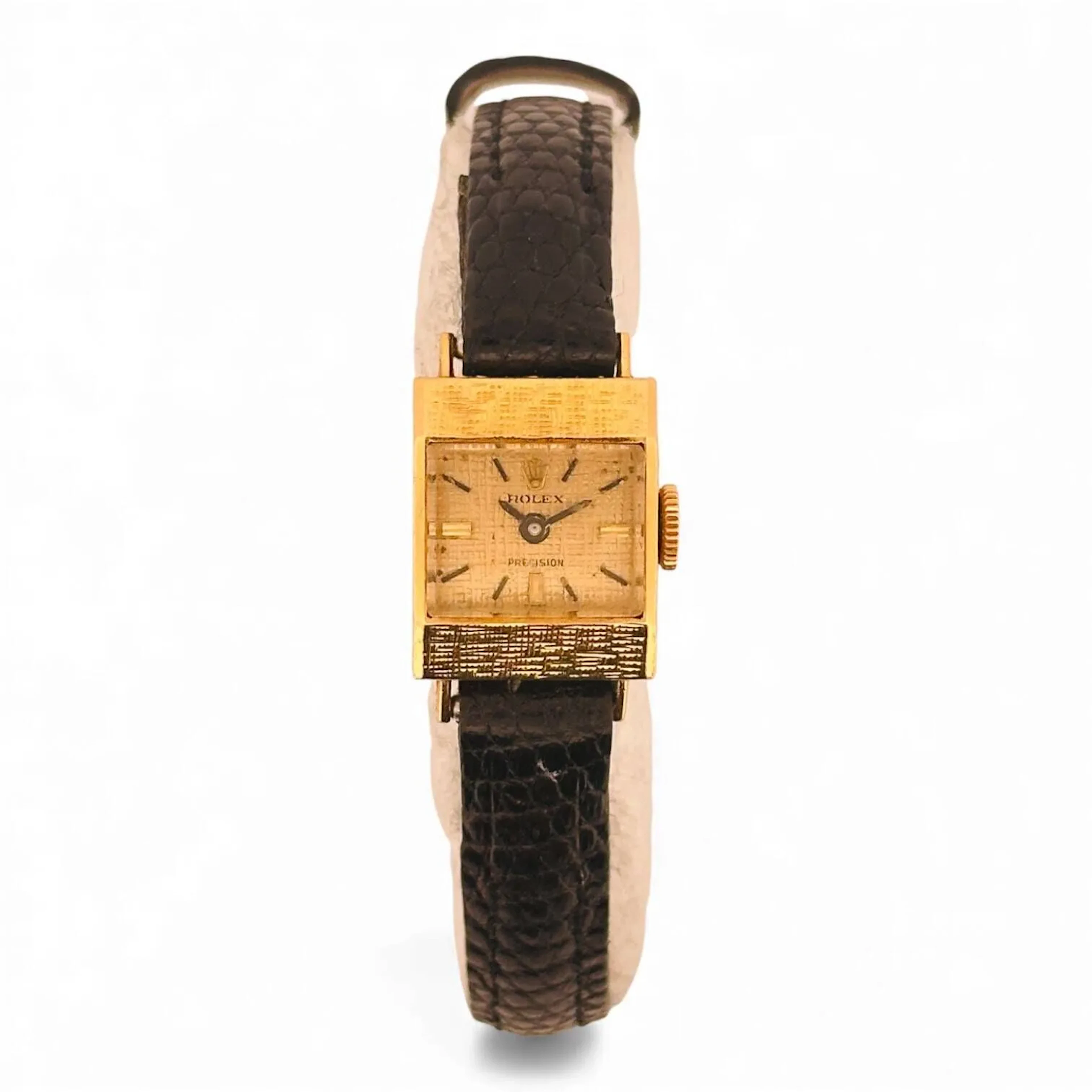 ROLEX PRECISION Montre bracelet de dame de forme en or 18K (750 millièmes), cadran doré soleillé décoré de ciselures verticales et horizontales, index en appliques dorées et noires, aiguilles fils bleuies. Lunette décorée de ciselures verticales et horizontales.Couronne signée Rolex. Fond clipé en or 18K (750 millièmes) signé Rolex, numéroté 1046304, à l’intérieur signé Rolex, référence 2161, fabrication Degoumois Henri (clé de Genève 7). Mouvement mécanique à remontage manuel signé Rolex. Bracelet en cuir noir, boucle ardillon en métal doré. Montre fonctionnelle lors de l’expertise, sans garantie de fonctionnement futur et d’état des pièces. Rayures au boitier et au verre, quelques légères traces au cadran. Accompagnée de son écrin d’origine. Vers 1964 Poids brut 11,7 g Dimensions 13 x 21 mm (corne à corne)