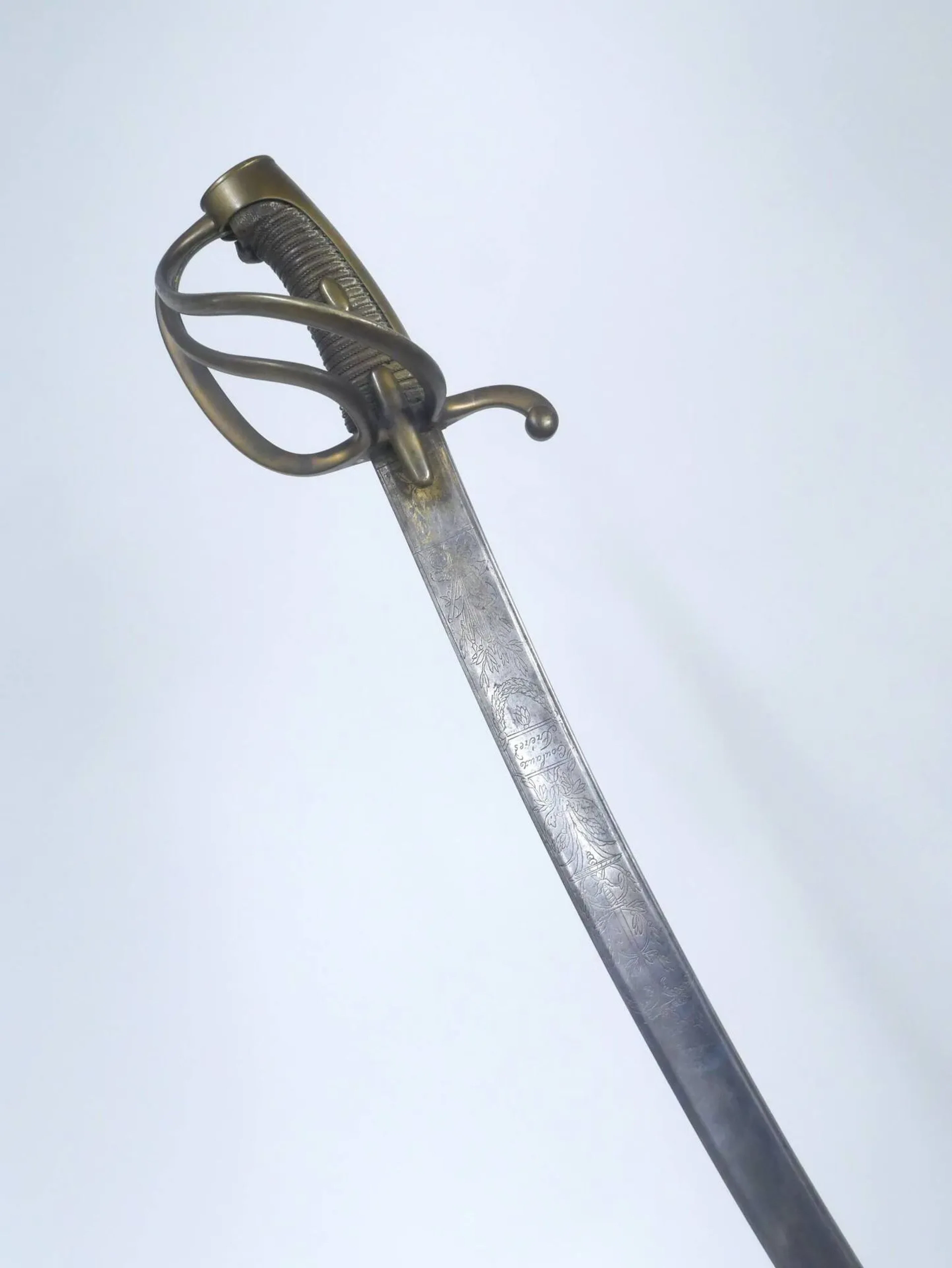 Sabre d’officier de cavalerie légère modèle AN XI, attribué à la Garde. Monture à la chasseur en laiton. Calotte à longue queue, arc de jointure dont se détachent deux branches. Croisière en navette et quillon courbe. Soie recouverte de cuir filigrané. Présence de deux oreillons. Lame courbe à gorge et contre-tranchant. Elle est gravée au tiers de l’aigle impériale, trophée et marquage de la manufacture de Klingenthal, Coulaux frères. Restes de dorure au talon. Fourreau en fer à deux larges bracelets laiton et pitons à facettes. Fortes oxydations. Longueur totale : 98 cm Époque premier Empire.