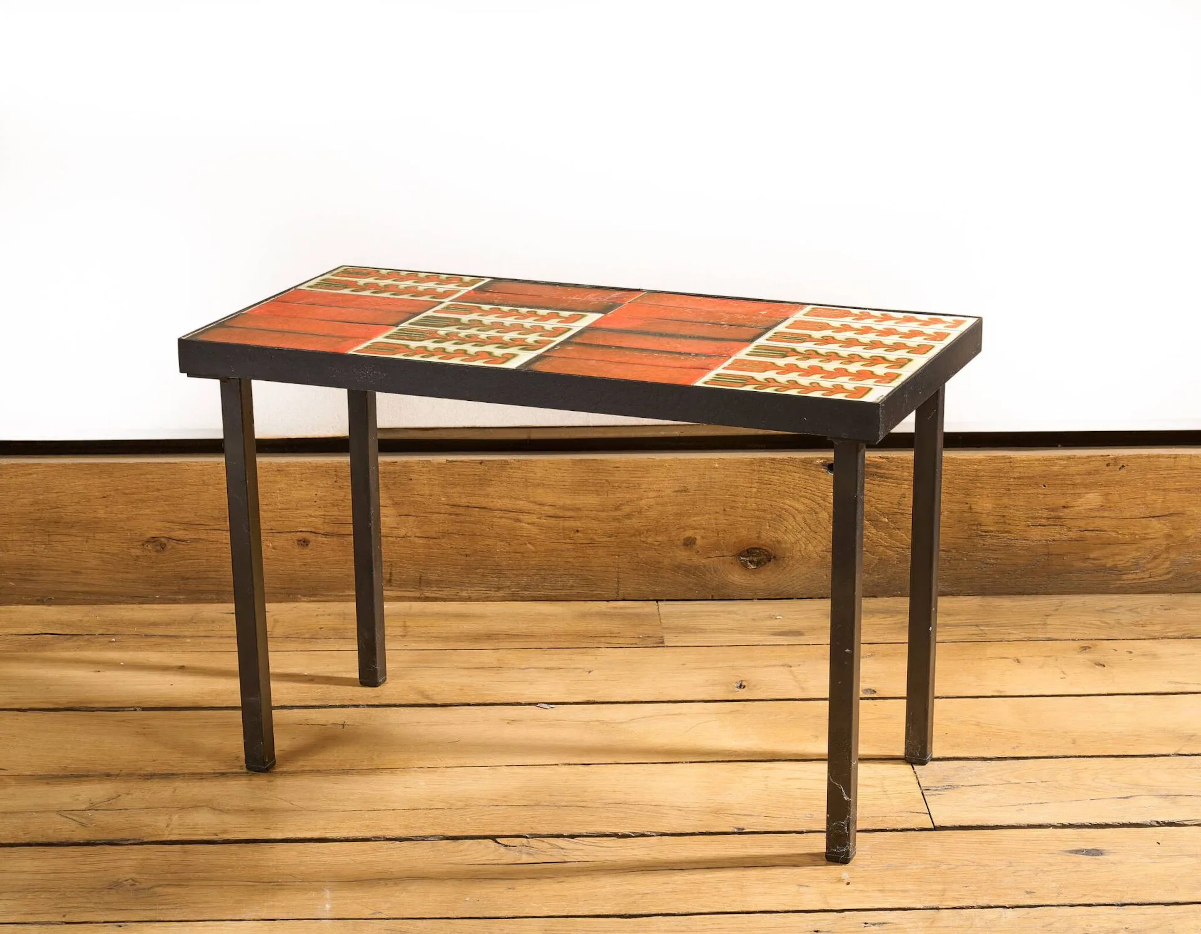 Roger CAPRON (1922-2006) Table basse modèle Palmettes de la série T, 1963, à plateau rectangulaire aménagé de carreaux de céramiques rouge orangé et blanc à décor de feuillages disposé sur une structure en métal laqué noir formant un piètement quadripode. Signée R. Capron dans un angle. H. : 39 cm. L. : 60 cm. - P. : 29.7 cm.