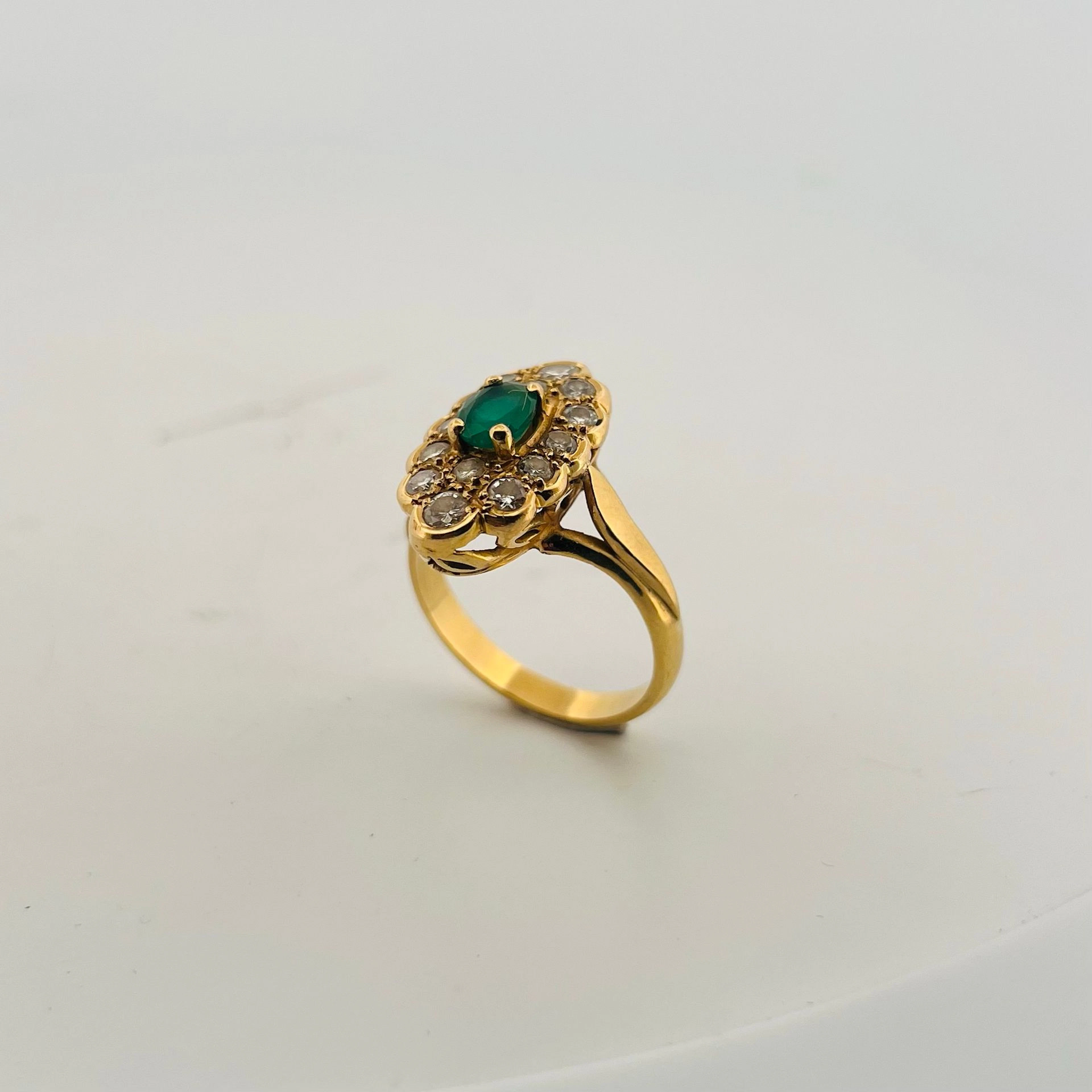 Bague marquise en or jaune 18K (750) sertie d'une émeraude ovale dans un entourage de diamants ronds taille brillant. Travail français. Tour de doigt : 62 - Poids brut : 8.31 g.