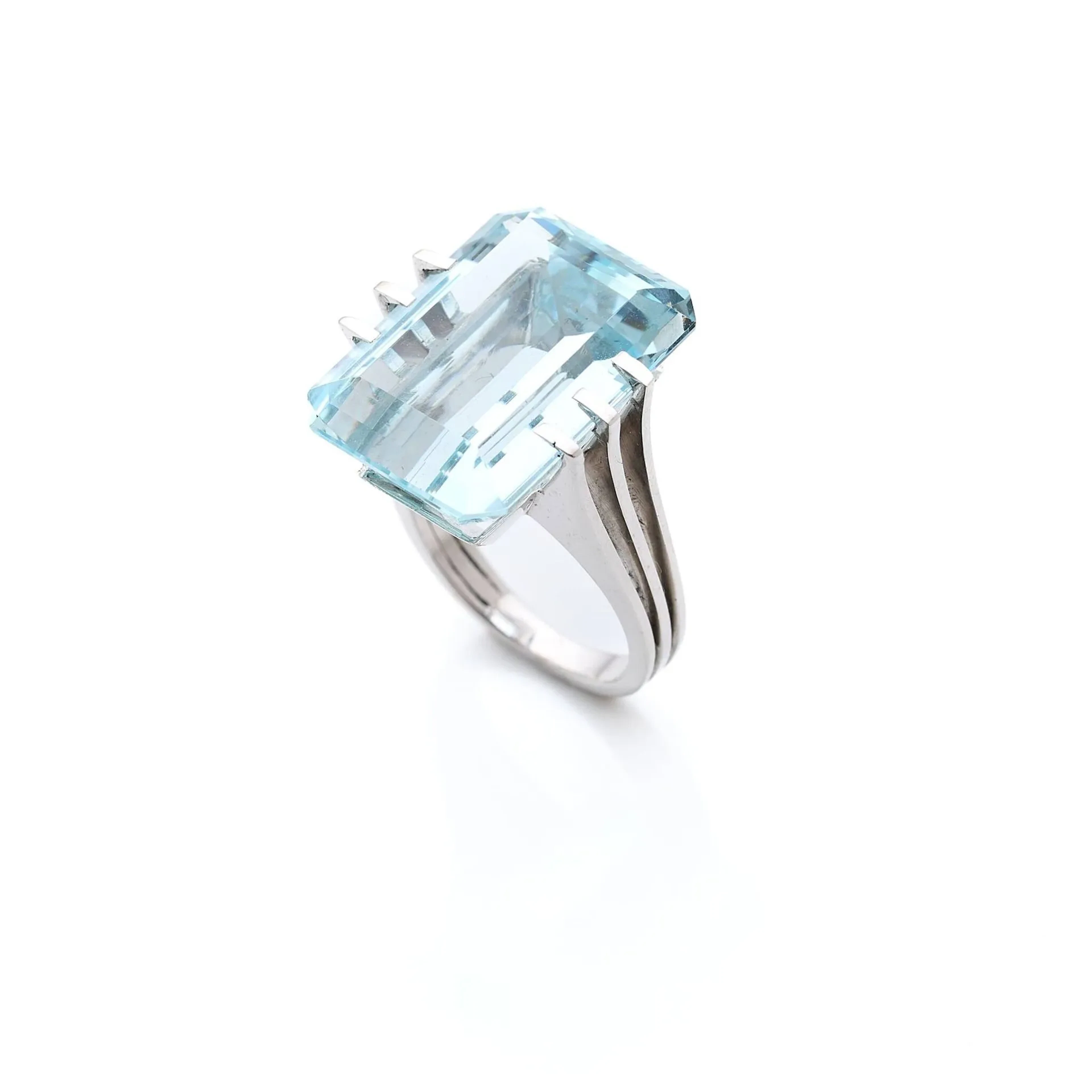 Bague cocktail en or gris 18k (750e), ornée d'une aigue-marine rectangulaire à pans coupés pesant environ 20 carats, la monture stylisée en fils. Travail français vers 1960/70. Poids brut : 11.70 g. Tour de doigt : 52.