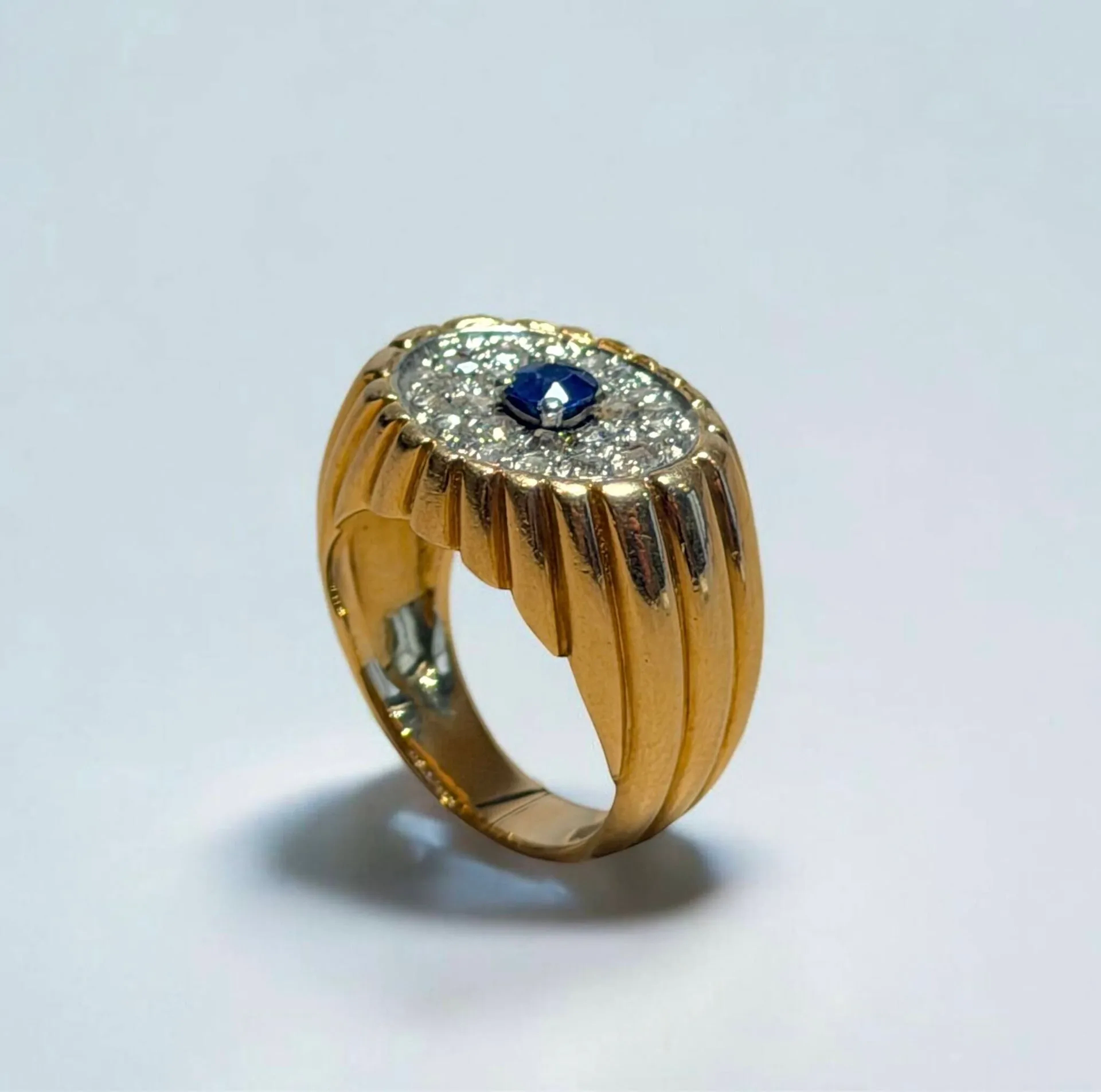Bague dome à godrons en or jaune et gris 18K (750 millièmes) centrée d’une pierre bleue dans un pavage de brillants Circa 1960 TDD : 55 Poids brut : 13.8 g Anneau recoupé
