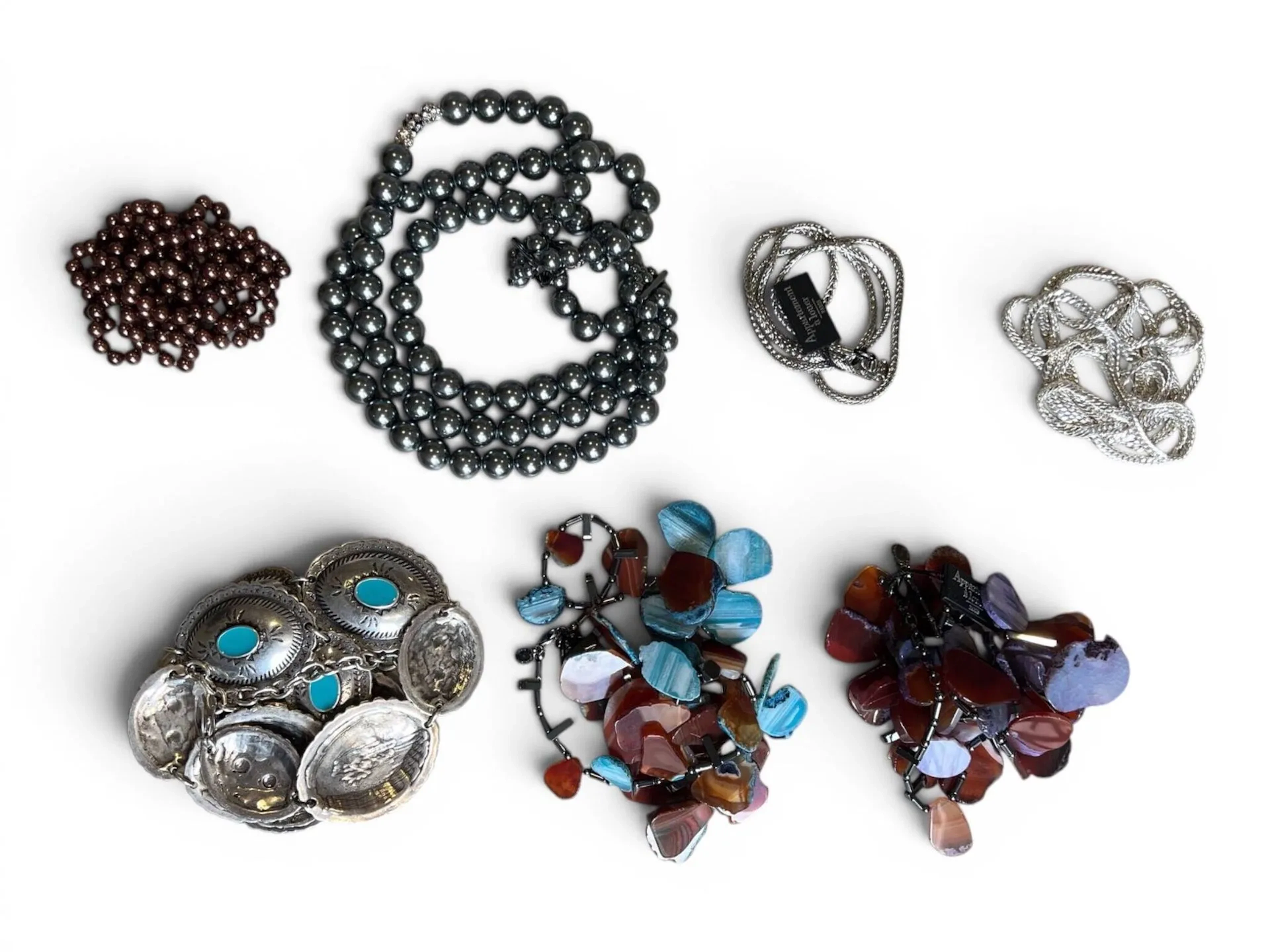 Lot de bijoux fantaisie comprenant : - un collier en perles tubulaires d'hématites et tranches d'agate brune ou bleue, ponctué de maillons rectangulaires en hématite. Signé Appartement à Louer. Longueur : 77 à 83 cm. - un collier en perles tubulaires d'hématites et tranches d'agate brune ou violette, ponctué de maillons rectangulaires en hématite. Signé Appartement à Louer. Longueur : 75 à 81 cm. - un sautoir en métal à maille palmier. Signé Appartement à Louer. Longueur : 86 cm. - un important collier à trois rangs de perles fantaisies grises, un rang ponctué de trois perles ornées de strass. Signé DEVERNOIS. Longueur : de 54 cm à 60 cm. - un long sautoir en métal à maille gourmette. Longueur : 170 cm. - un long sautoir de perles fantaisies brunes. Longueur : env. 140 cm. On y joint une ceinture en argent (800 min) formée de maillons ovales ciselé et décoré d'émail à l'imitation de la turquoise. Longueur : jusqu'à 100 cm. Poids brut : 414 g;