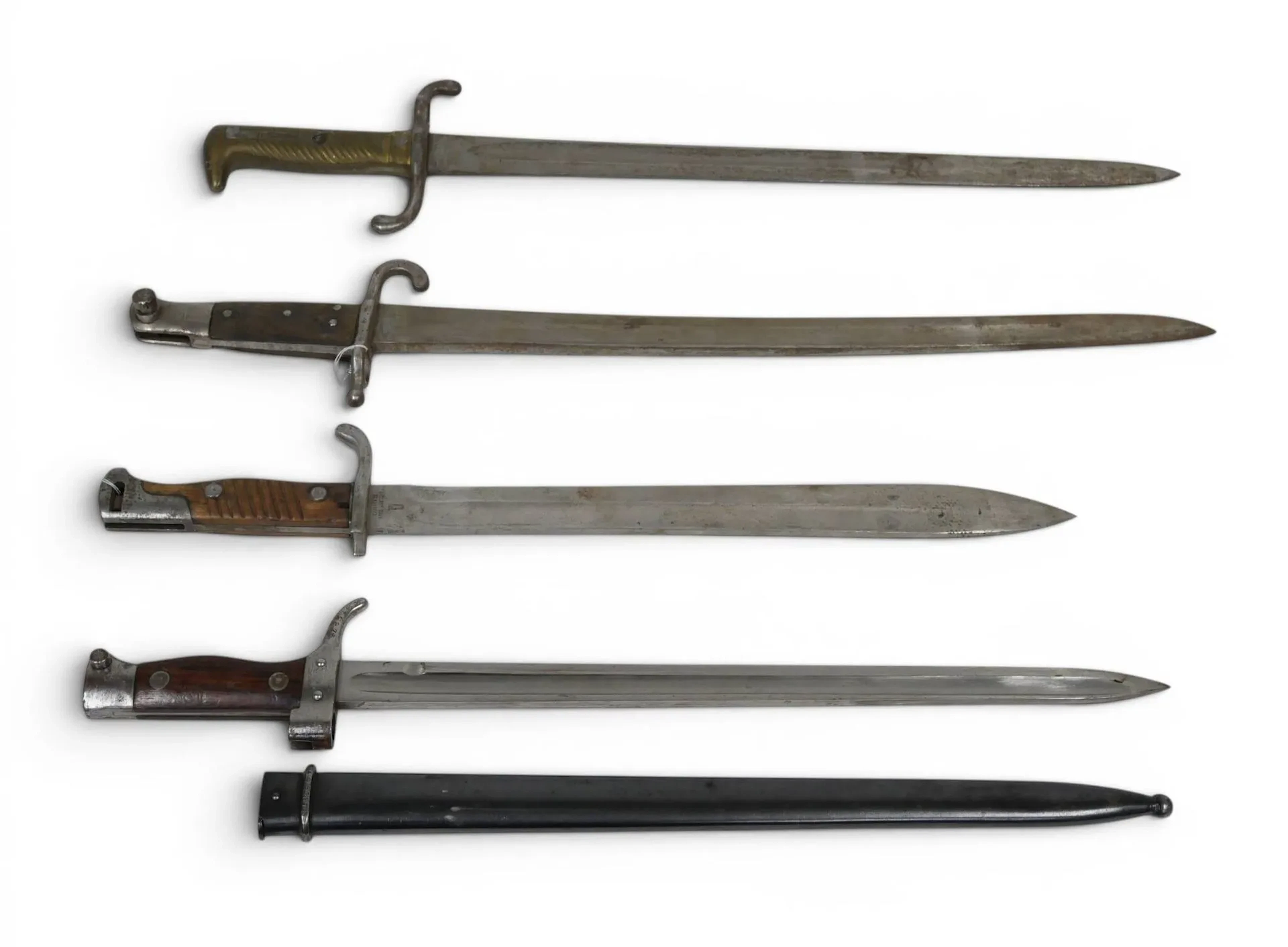 Quatre baïonnettes : - française modèle Berthier, avec son fourreau. Mono matricule : croisière et fourreau n° 52875. L. : 51 cm. - allemande modèle Mauser 98 k Josua Corts, sans fourreau. L. : 49.60 cm. - allemande modèle 1871 Coulau & C Kligenthal de 1878, sans fourreau. L. : 58.30 cm. - une baïonnette sans fourreau, lame gravée GF. L. : 60 cm.
