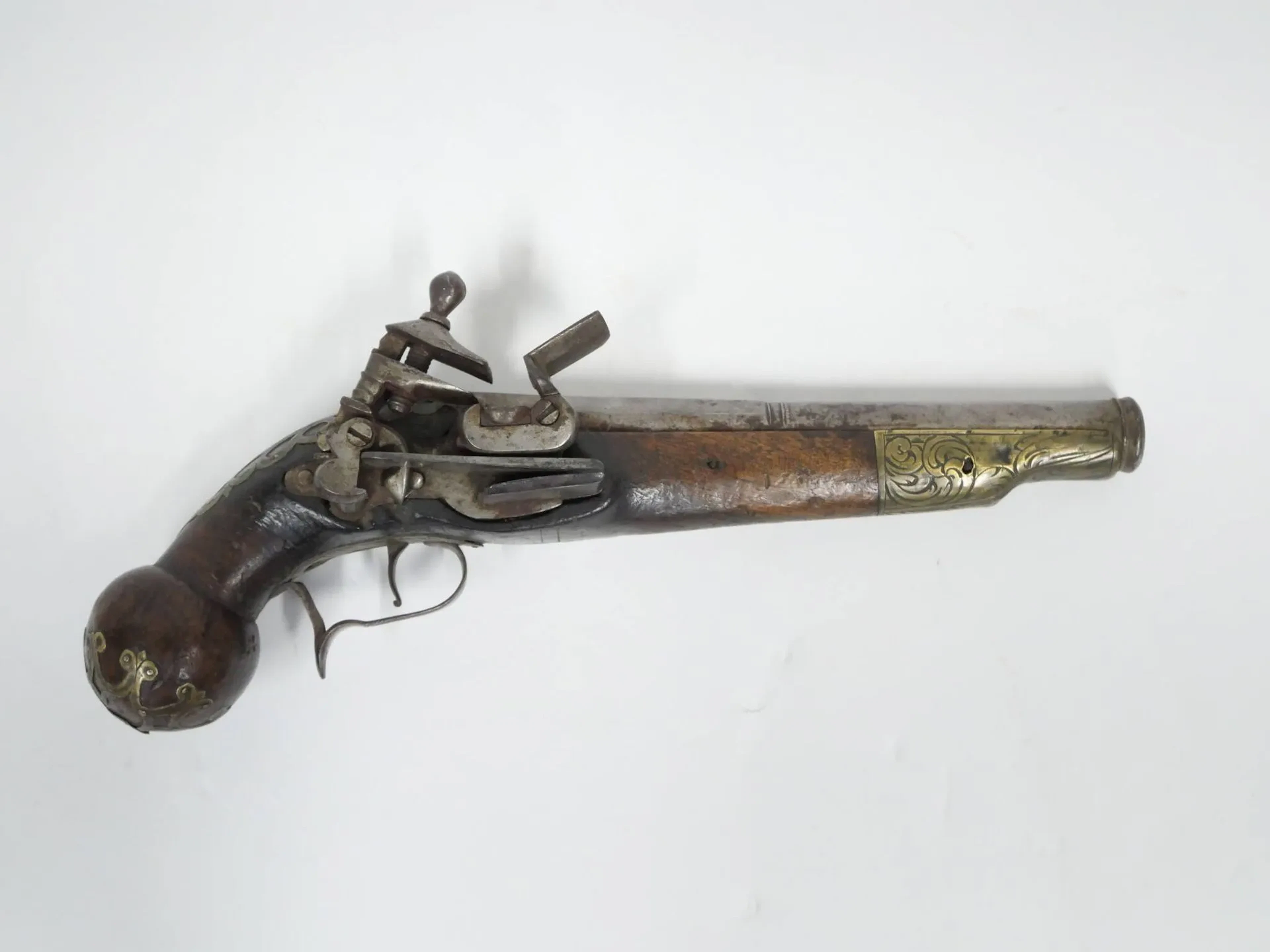 Pistolet à silex napolitain. Platine à la miquelet et canon à double registres à pans puis rond. Poinçonné au tonnerre « MAPI » et d’une fleur de lys sur le pan supérieur. Crosse en noyer et garnitures en laiton découpé et ciselé. Pontet et contre-platine en fer. Bonne mécanique. Longueur totale : 31 cm. Naples, XVIIIe siècle.