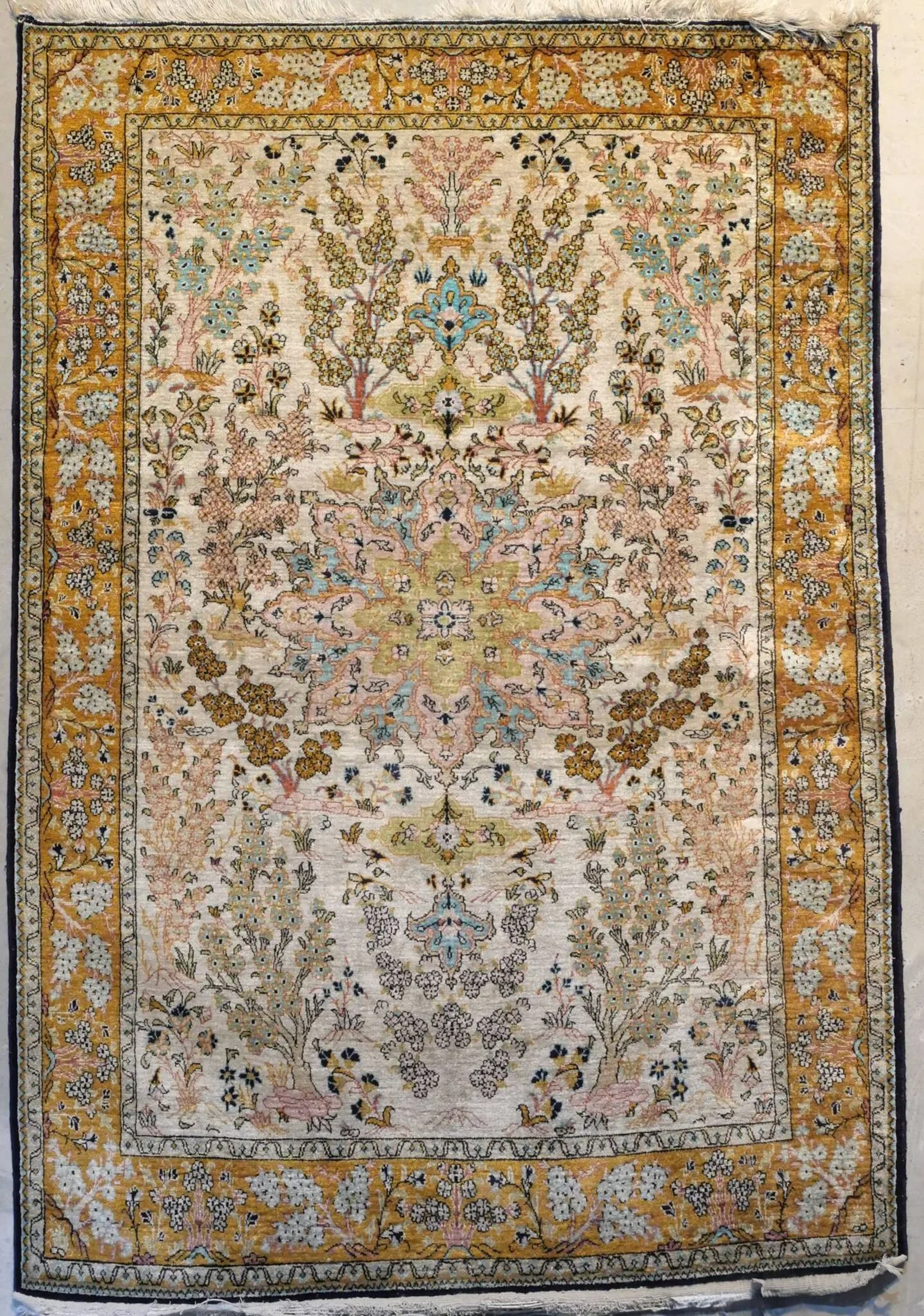 Original et fin Ghoum en soie Iran Époque du Shah Vers 1965 Dimensions 163 x 110 cm Velours, chaînes, trame et franges en soie 100% en soie Densité env 8/9000 nœuds au dm². Bon état général Belle finesse Champ ivoire à original décor de semis de plantes et arbustes de vie fleuris à tonalités pastels encadrant une rosace centrale vieil or, vieux rose et bleu ciel à fleur étoilée. Triple bordure dont la principale jaune d'or à décor de rangées de brins de fleurs et feuillages finement dessinés Bibliographie : Andrew Middleton, Roger Bechirian, Edwin Gans-Ruedin
