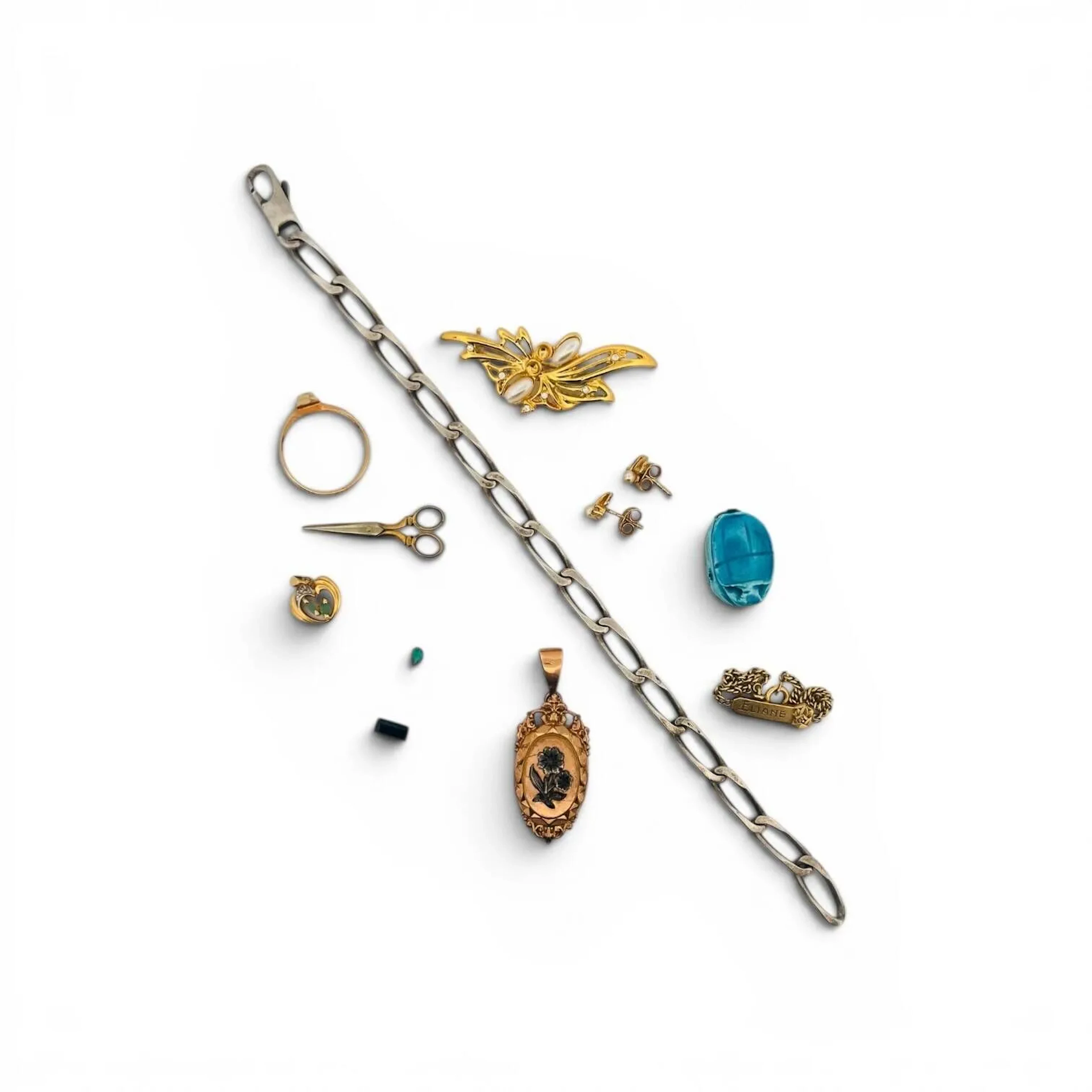 Lot de bijoux divers comprenant : - un pendentif cœur en or 18K (750) serti de deux émeraudes navettes. Poids brut : 1.04 g. - une paire de clous d'oreilles en argent (925) doré, chacun orné d'une pierre blanche et d'une perle fantaisie. Poids brut : 1.15 g. - une gourmette en argent (925). Poids : 11.79 g. - une bague navette en métal doré décoré de résine bleue. Tour de doigt : 57 - deux pierres sur papier dont un saphir synthétique rectangulaire à pans vifs. - une gourmette en métal doré retenant une plaque nominative. - une broche gerbe en métal doré retenant des pierres blanches et perles fantaisie - un pendentif secret en métal appliqué de fleurettes - un scarabée d'Egypte - une paire de ciseaux miniature