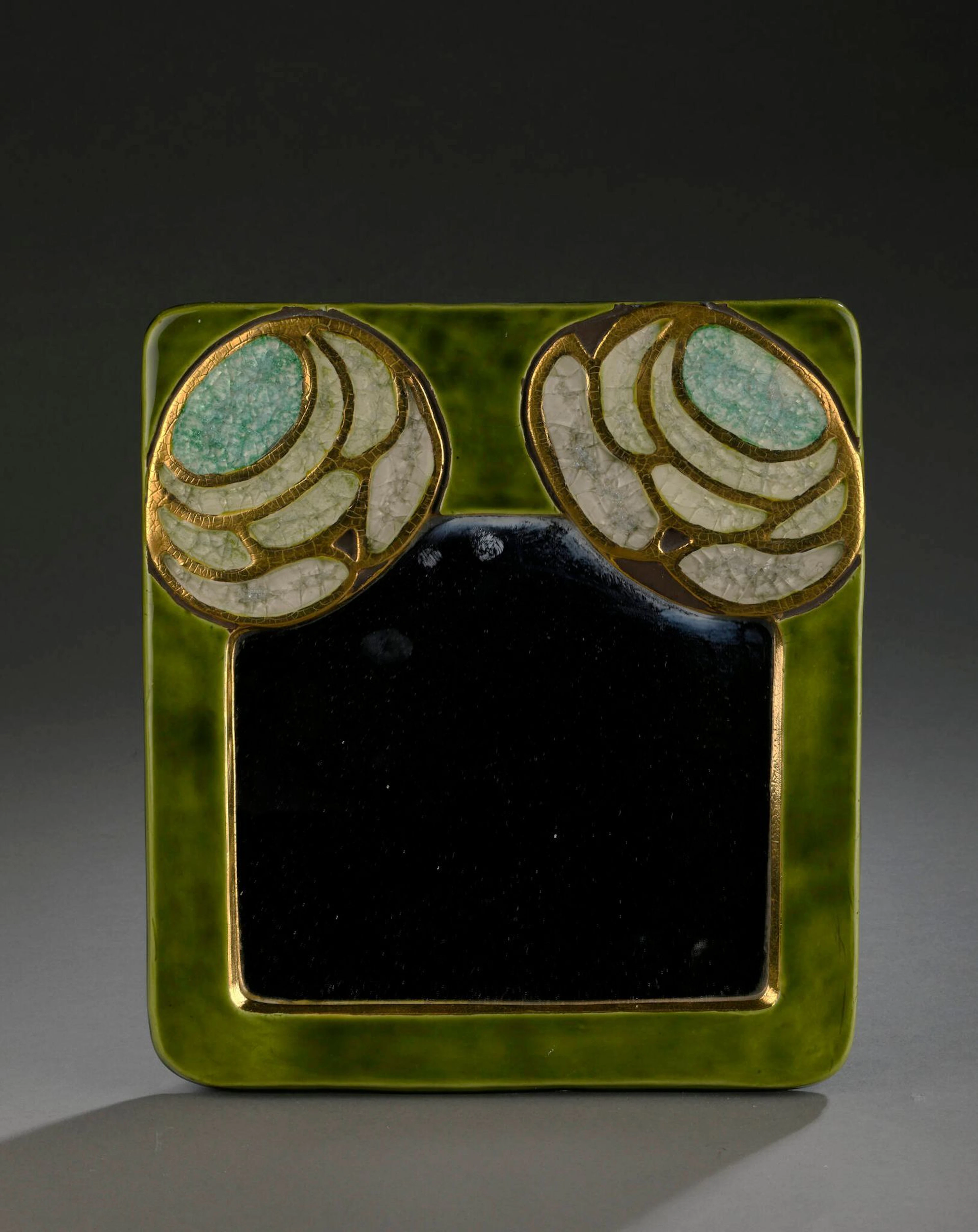 Mithé ESPELT (1923-2020) Miroir mural modèle Arts décoratifs, circa 1980 Épreuve en terre estampée et émaillée vert, or craquelé et verre cristallisé H. : 30.5 cm. L. : 27.5 cm. (Usures et taches à la feutrine au dos) Bibliographie : - Antoine Candau, Mithé Espelt - le luxe discret du quotidien, Edition Odyséee, 2020, modèle similaire reproduit p. 181