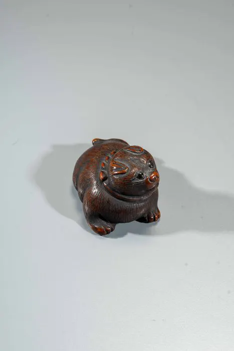 A finely carved boxwood netsuke depicting a crouching dog...