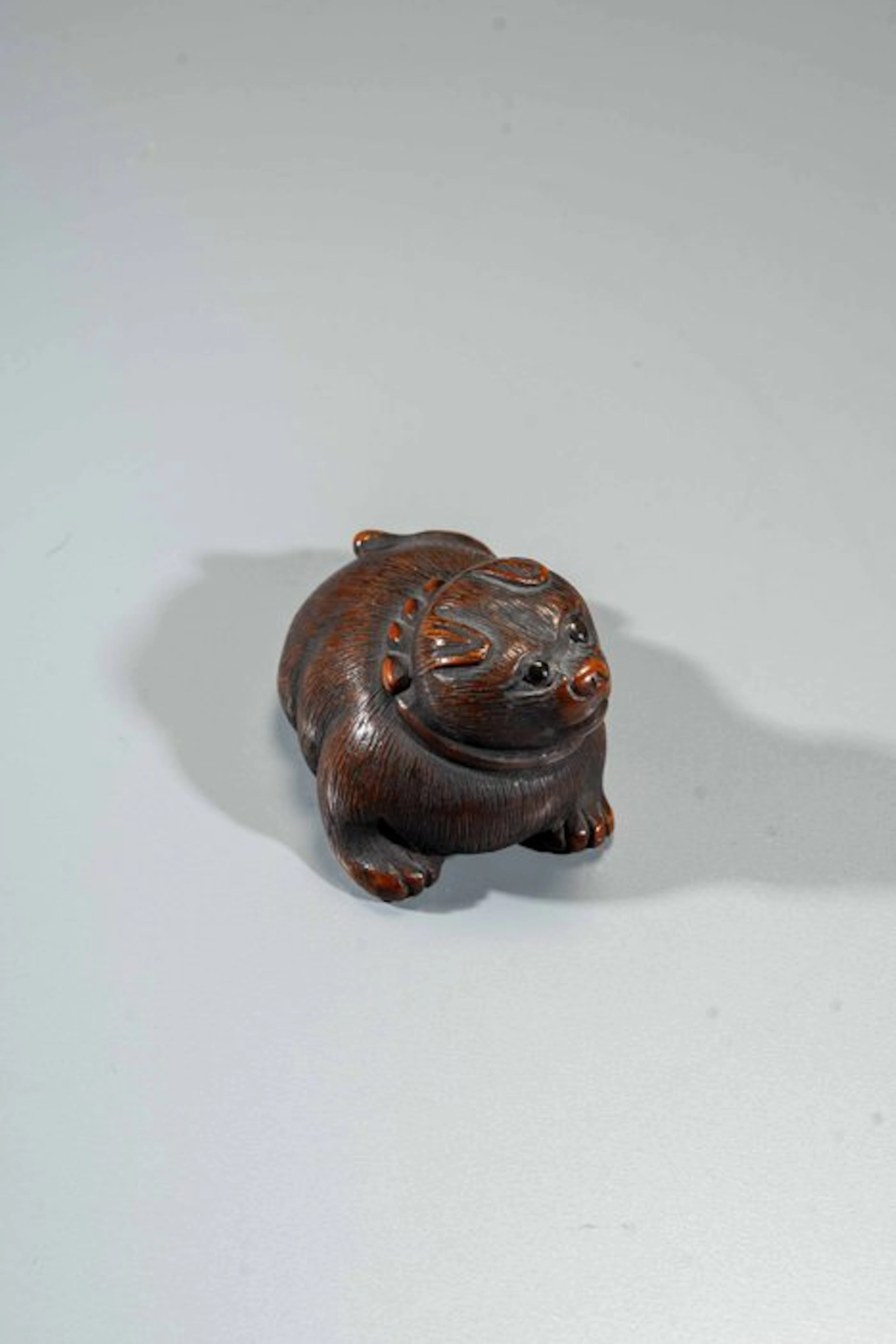 A finely carved boxwood netsuke depicting a crouching dog...