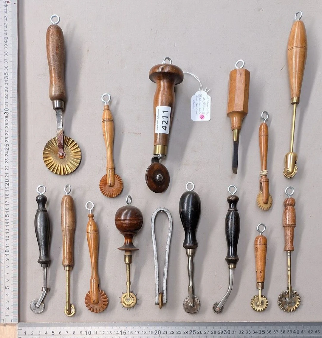 15 different dough cutters made of steel, brass, and wood on an oak