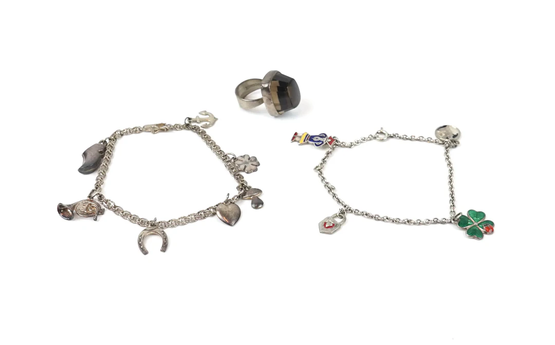 Pulseras, 2 con amuletos y un anillo con piedra color humo, plateada.