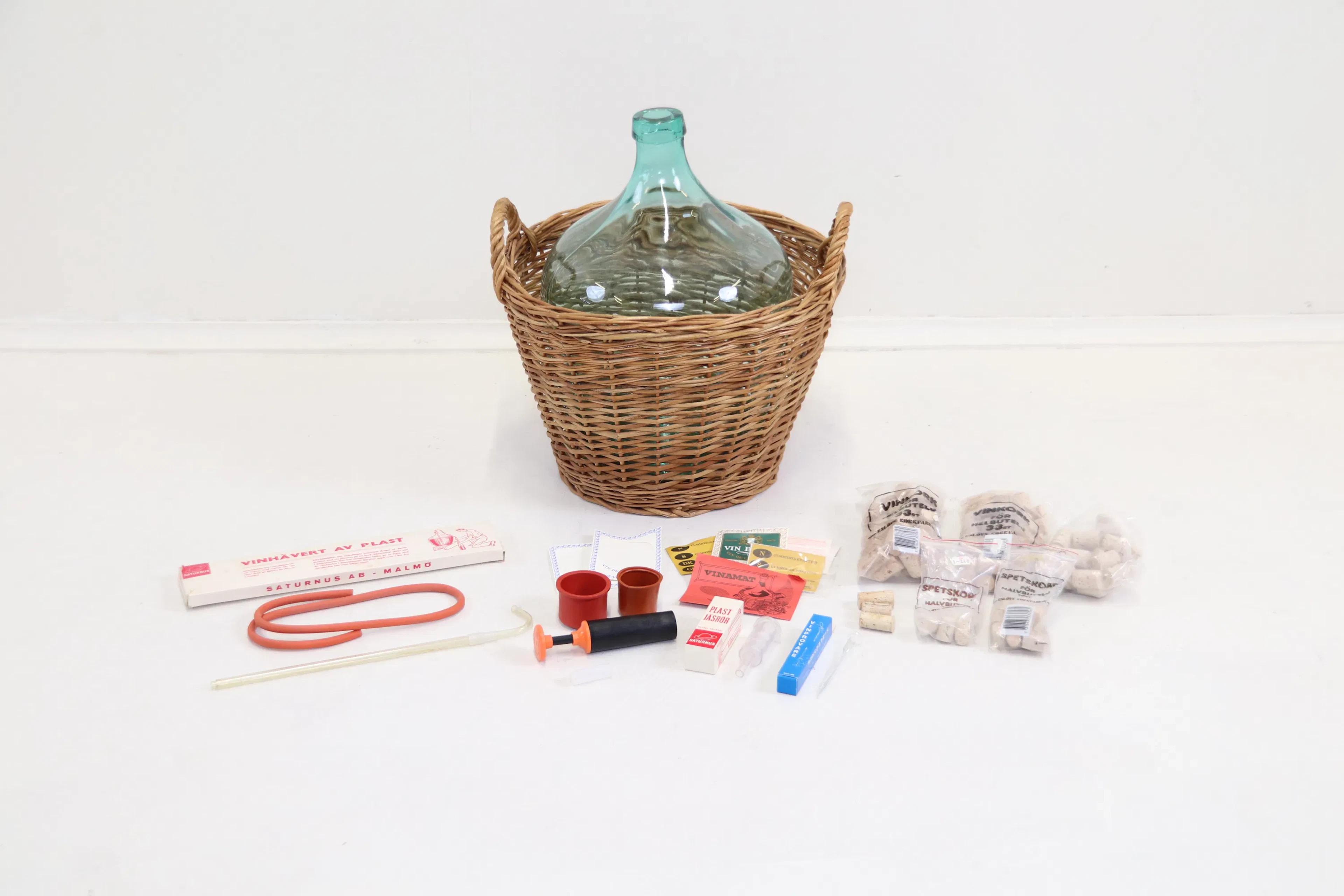 Ladies' jeanne, glass, in basket, and accessories for winemaking.