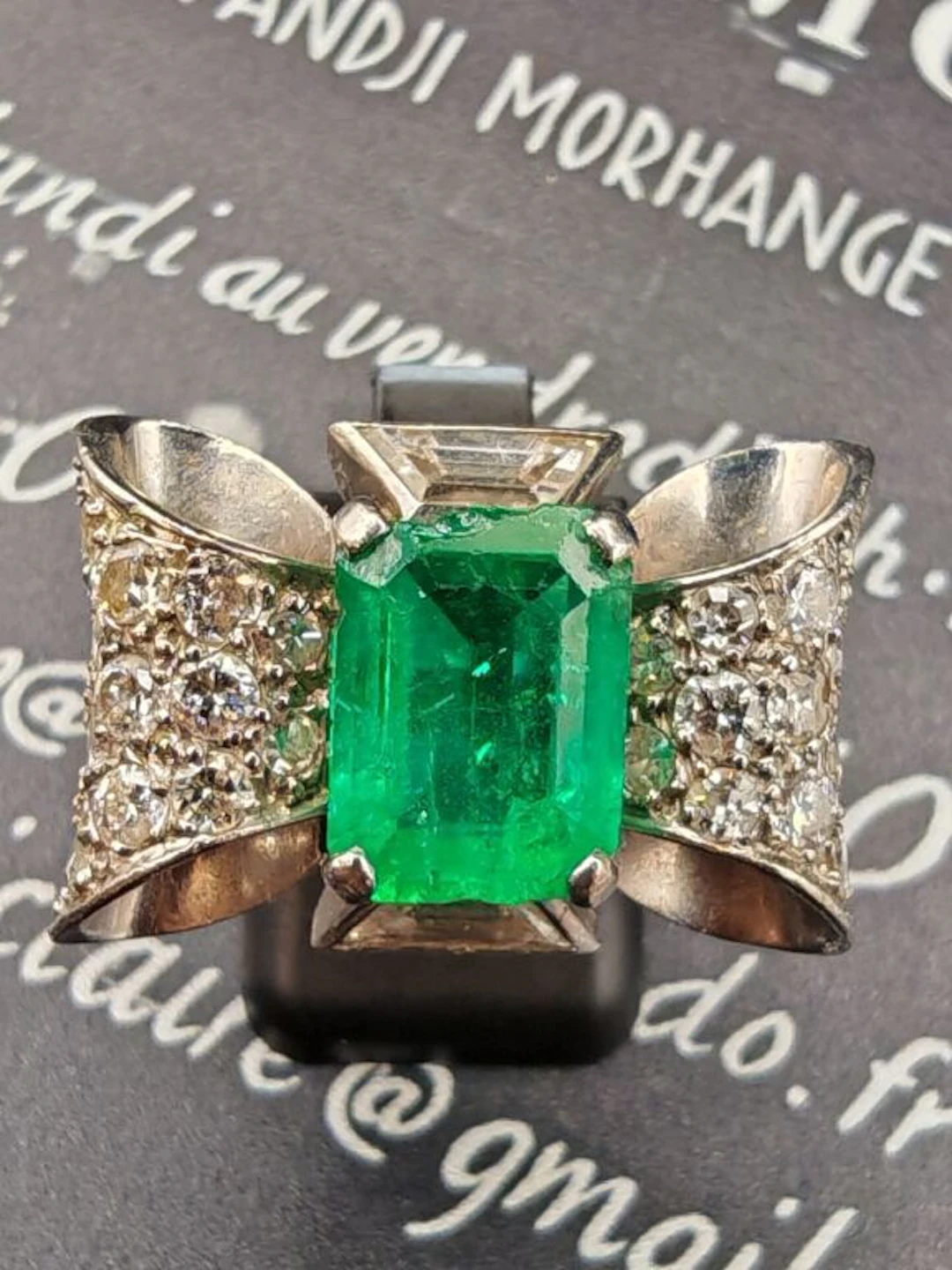 Platinum bow-knot ring, set with a center emerald—likely from Colombia—in