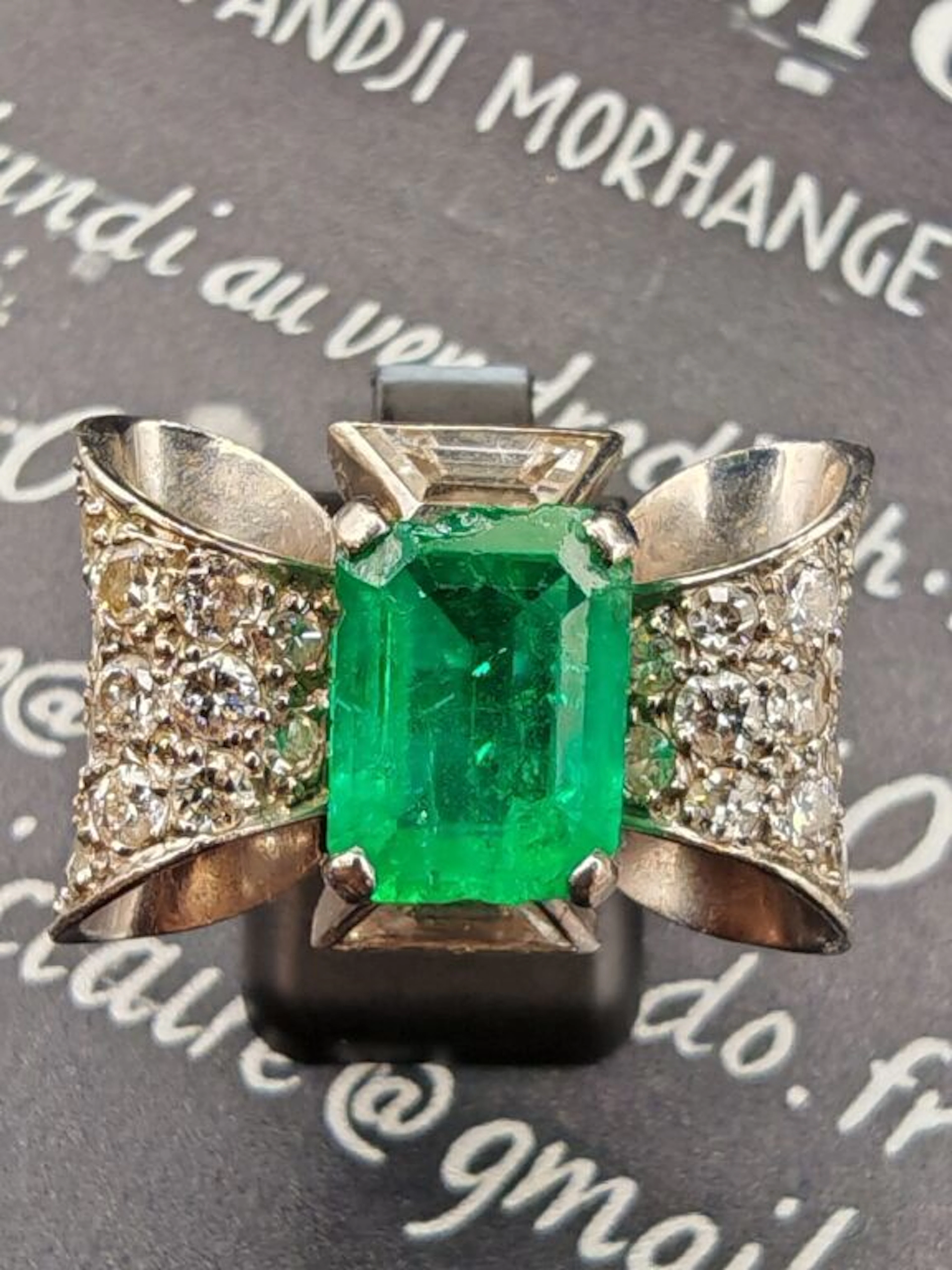 Platinum bow-knot ring, set with a center emerald—likely from Colombia—in