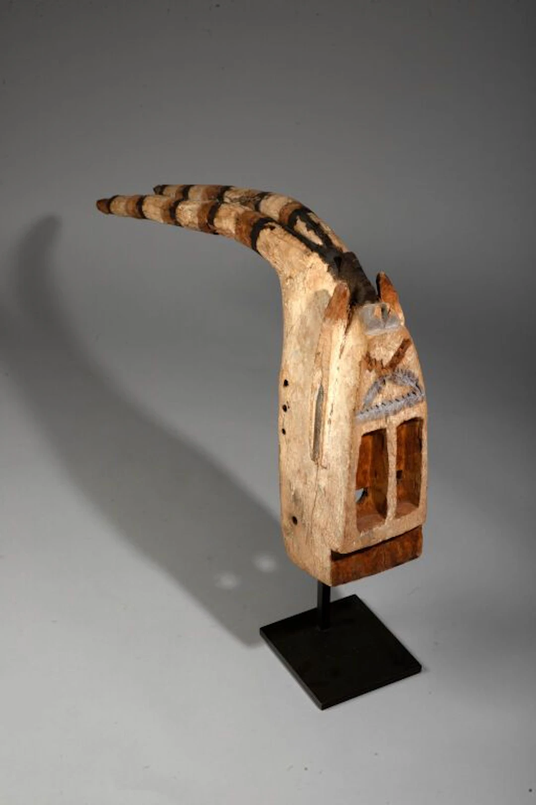 Antelope mask with long horns curved backward. The face is rendered