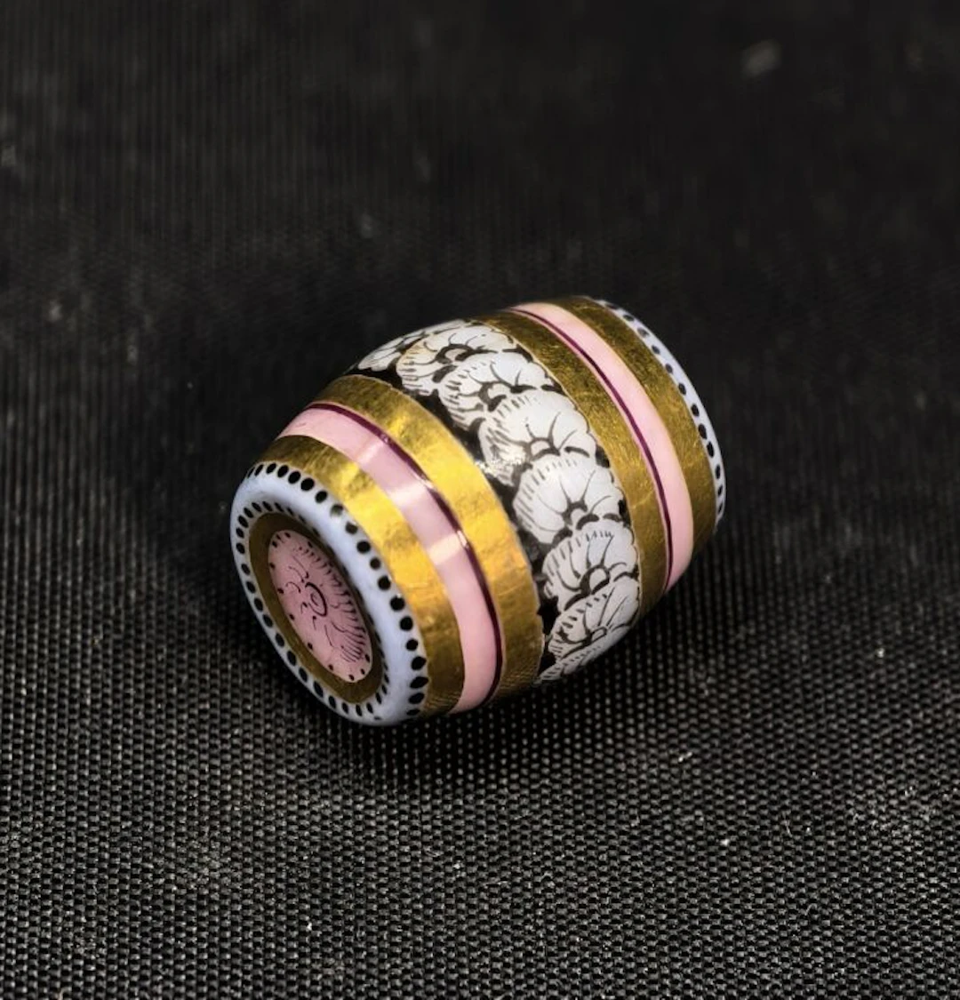 A charming porcelain charm featuring a fully hand-painted barrel with