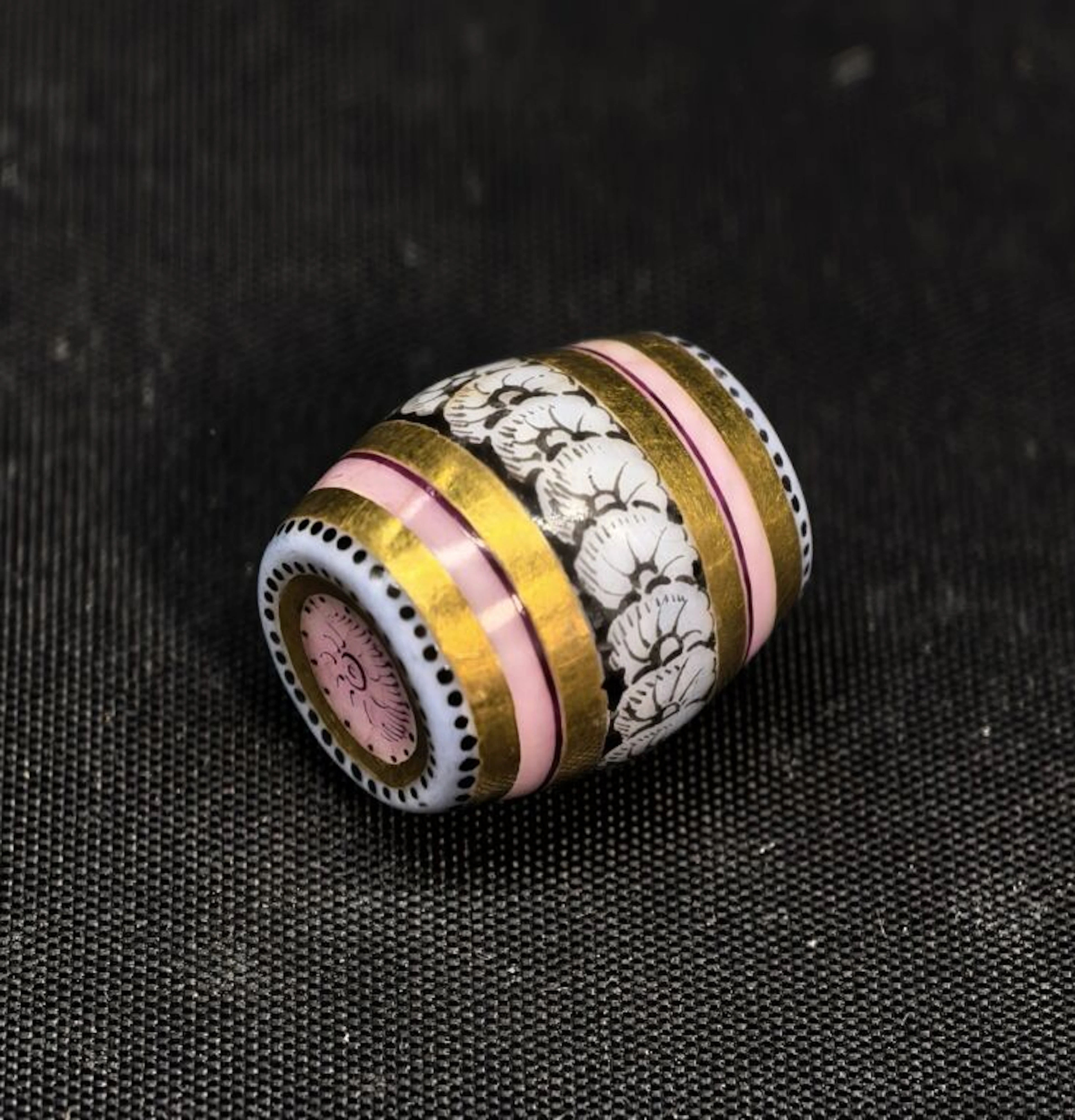 A charming porcelain charm featuring a fully hand-painted barrel with