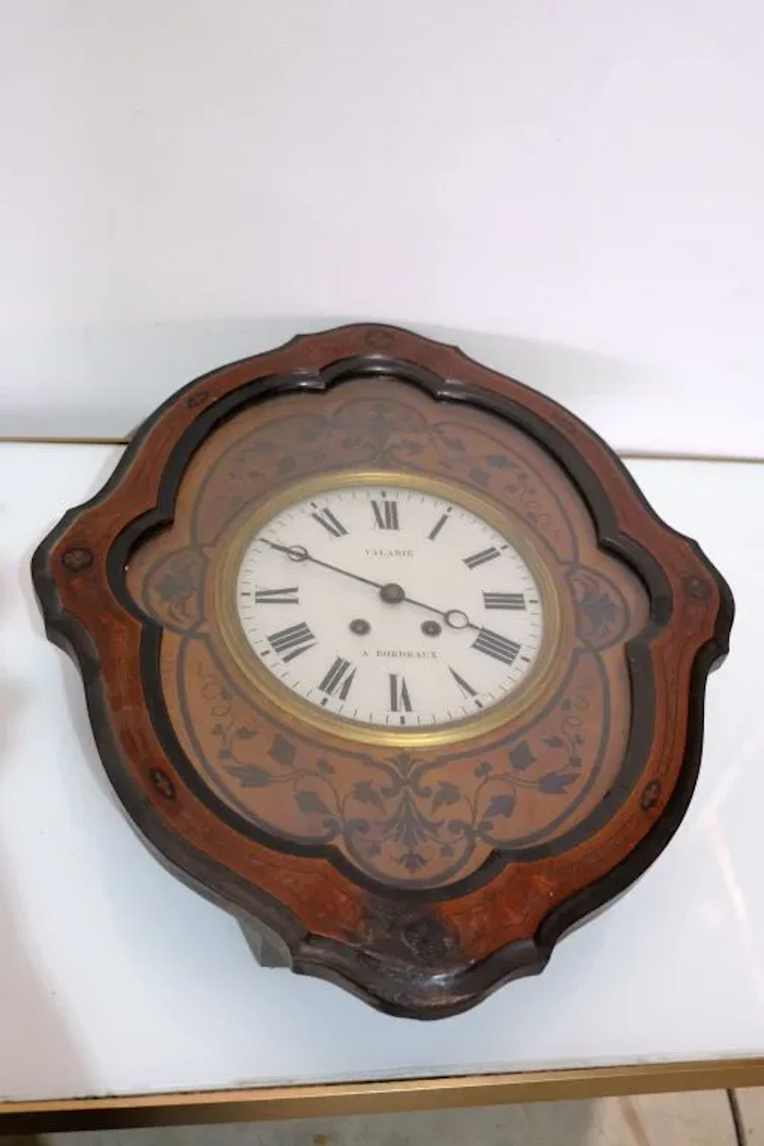 Wood veneer wall clock with inlaid foliage and interlaced patterns.