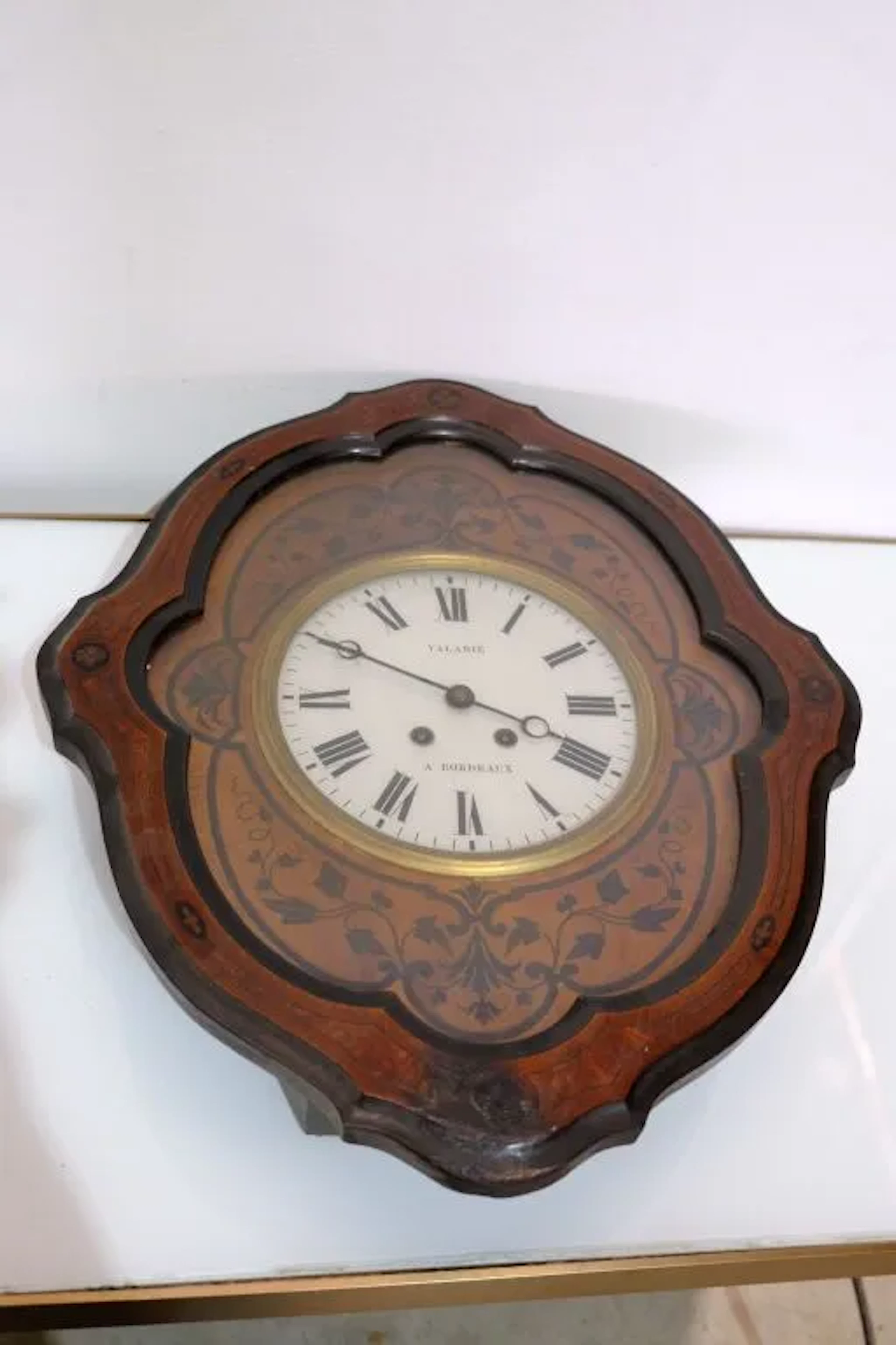 Wood veneer wall clock with inlaid foliage and interlaced patterns.