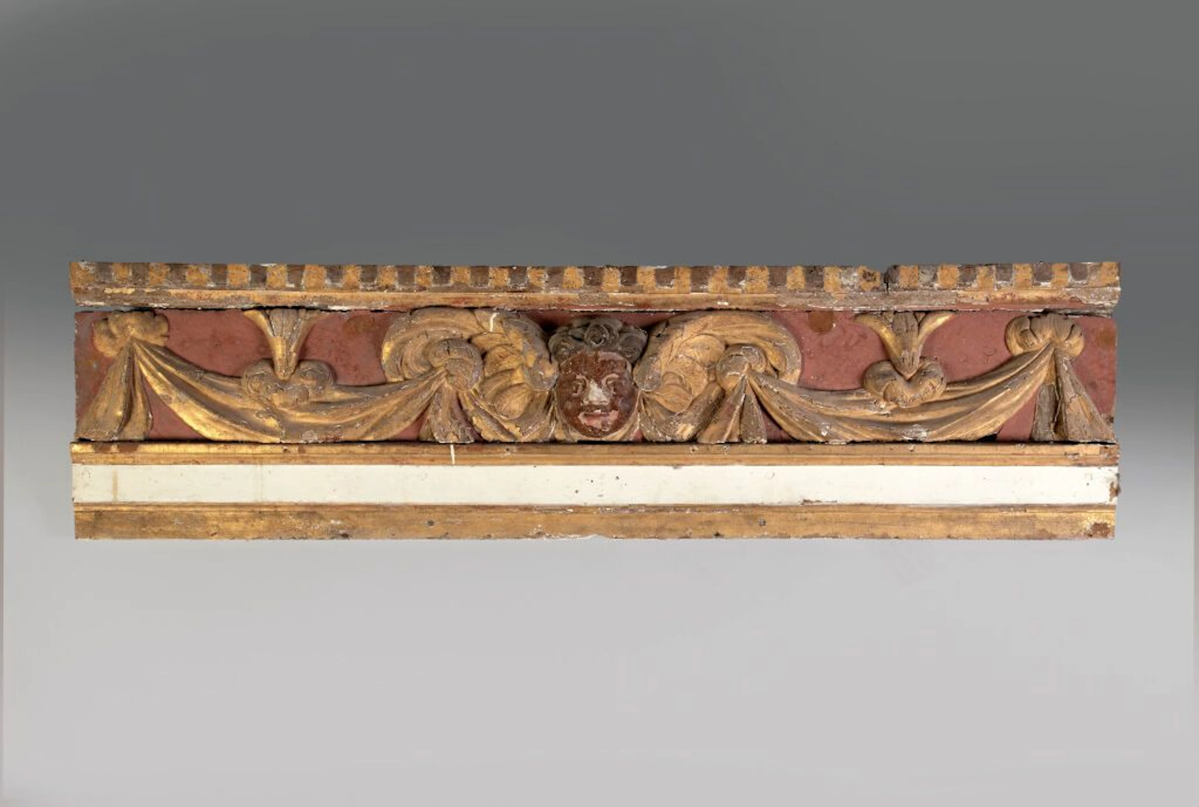 A carved and gilded wood panel, repainted in ochre and white, decorated