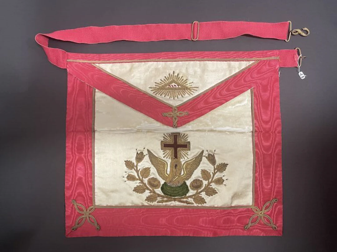 Cream-colored silk apron, red moiré fabric, and gold thread. In the