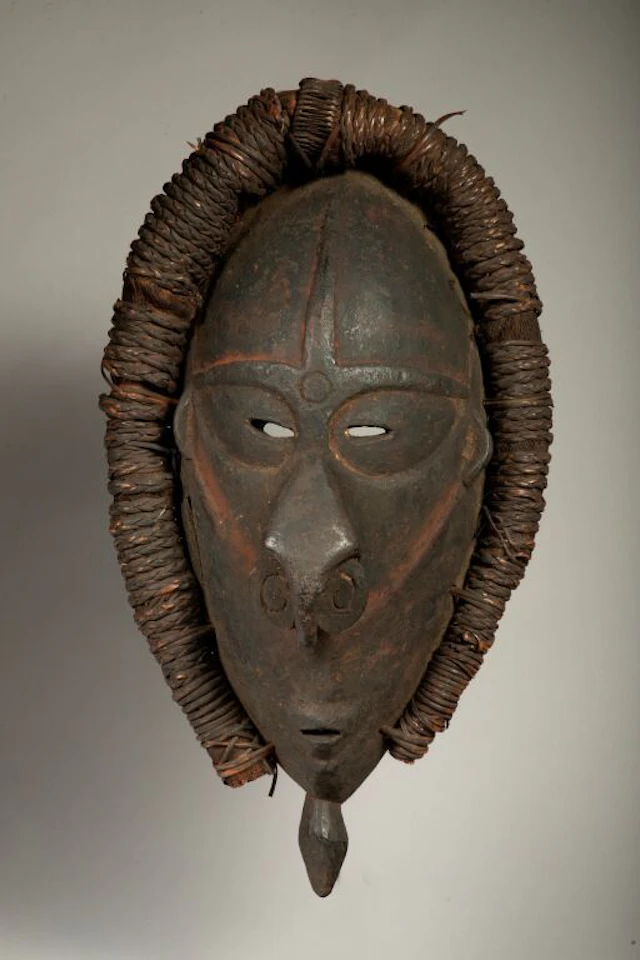 Mask with a handle surrounded by a plant-motif rim. The rounded nose