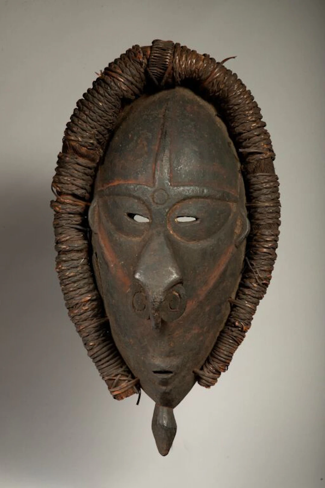 Mask with a handle surrounded by a plant-motif rim. The rounded nose