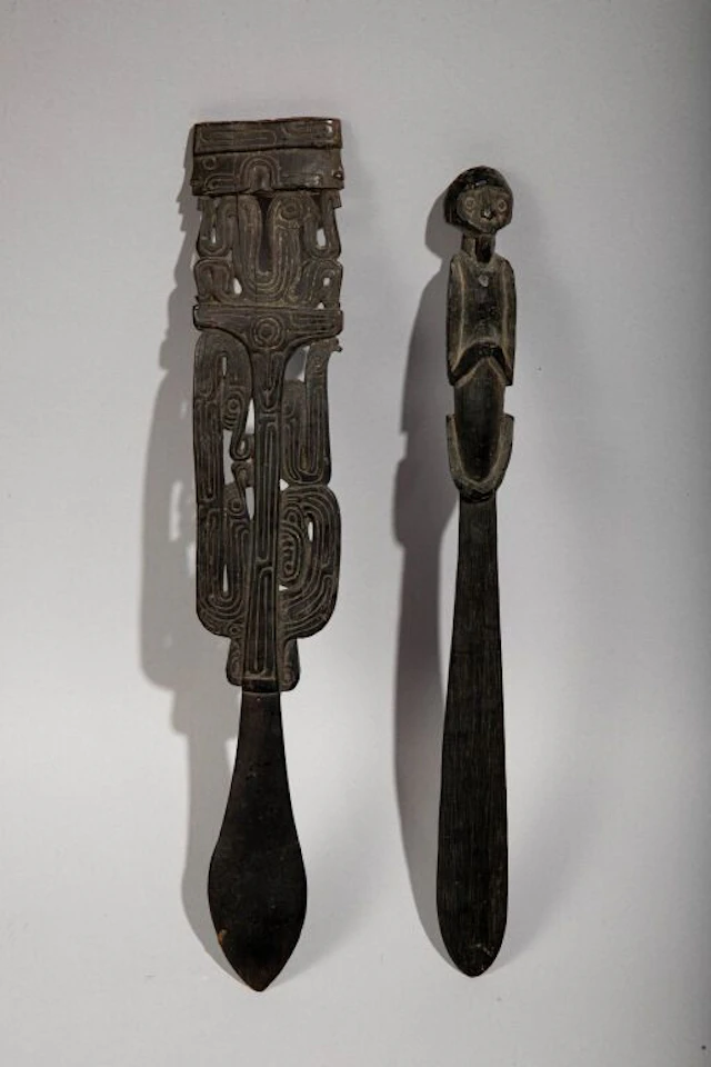Two lime spatulas, one featuring a seated figure, the other featuring