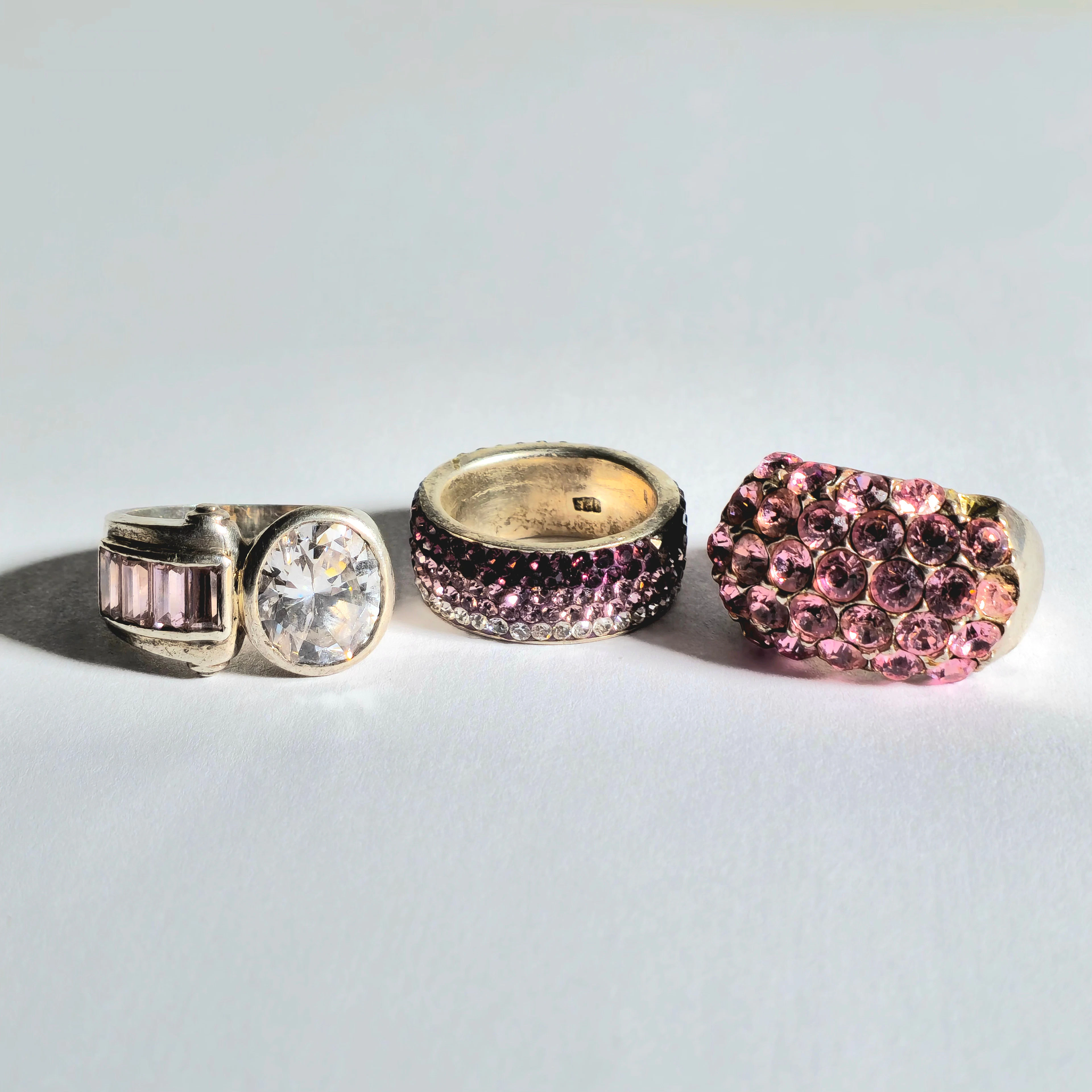 TRES ANILLOS EN PLATA CON CIRCONITAS DE COLOR ROSA, BLANCO Y LILA.