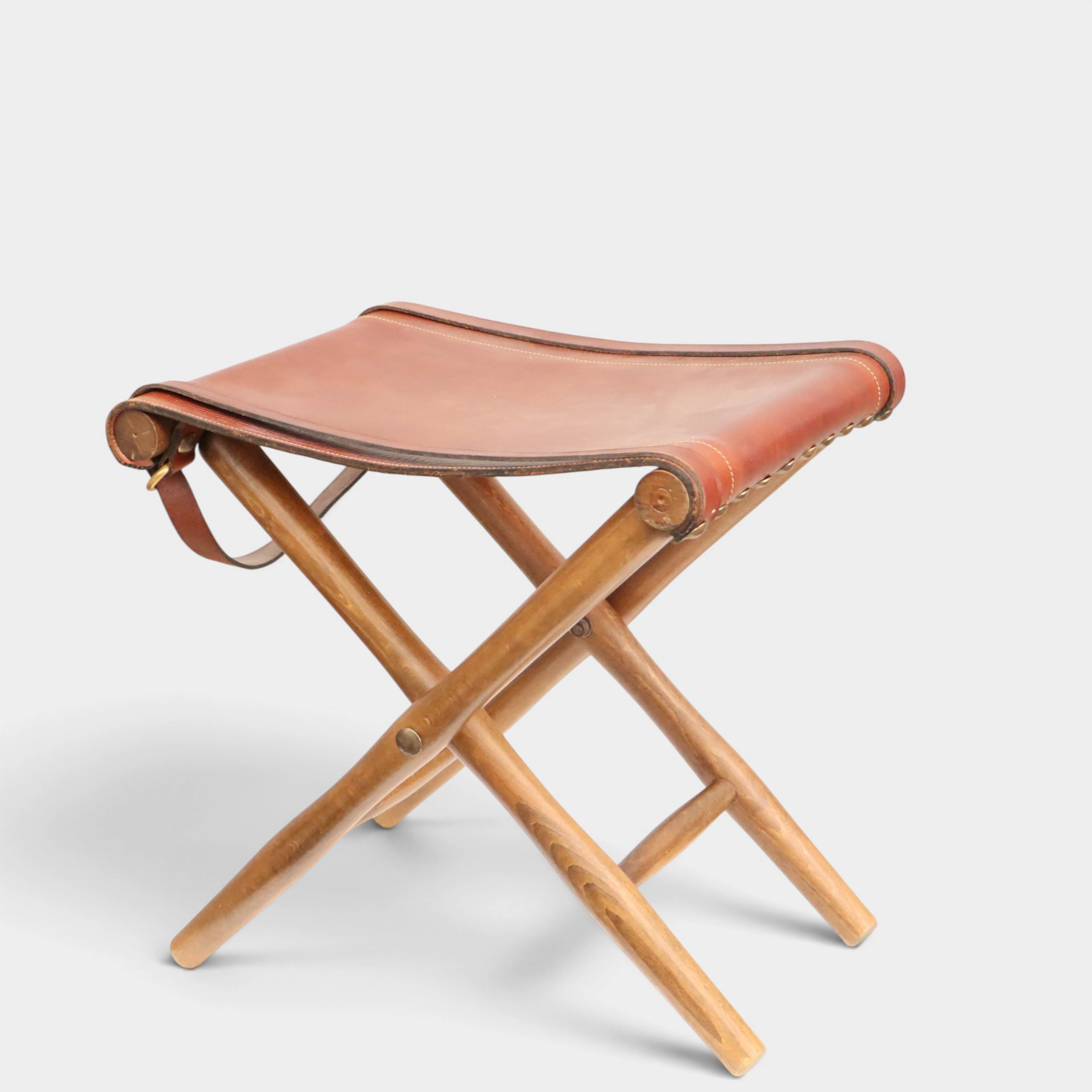 Taburete de safari en forma de tijera con asiento en cuero.
