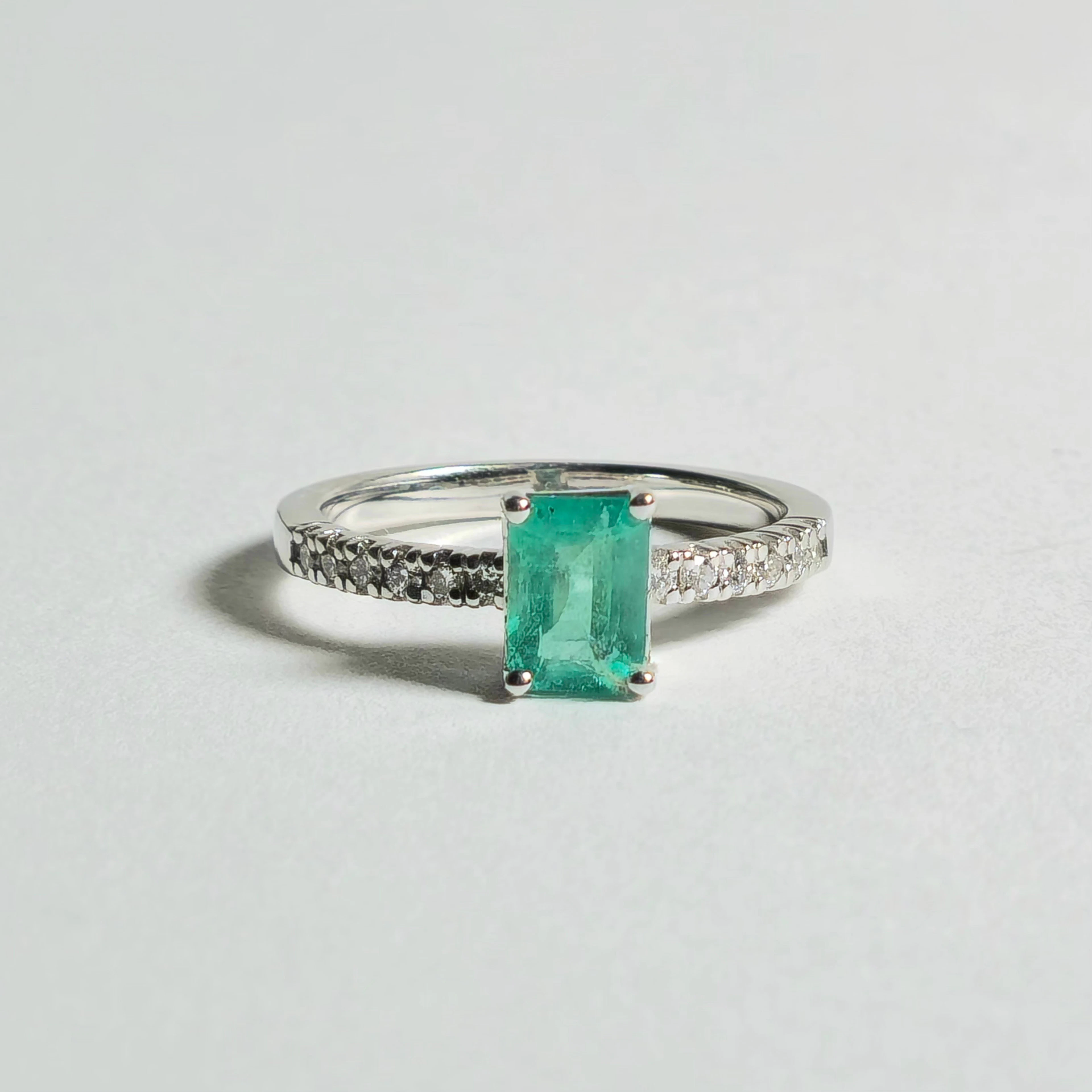 ANILLO EN ORO BLANCO 18 QUILATES CON ESMERALDA 0,70 KT ORLADO POR DIAMANTES.