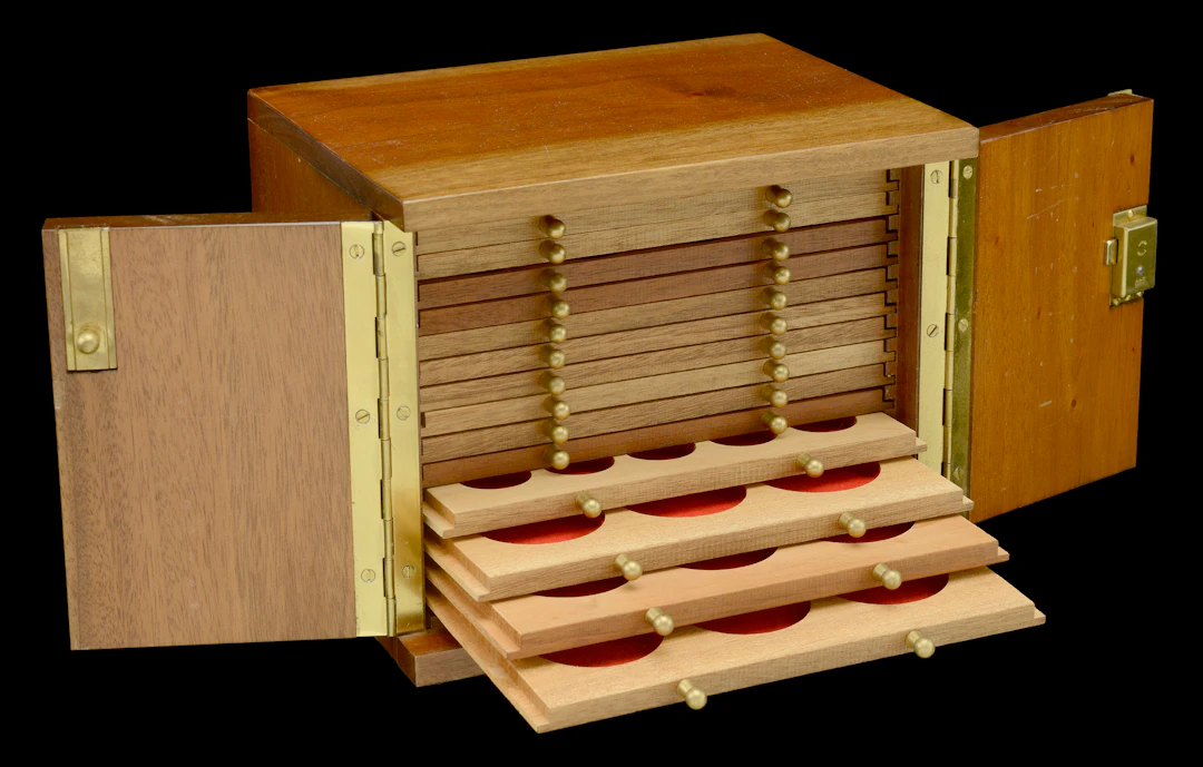 A wooden coin cabinet by Peter Nichols, 22 x 17.5 x 17.5 cm, comprising